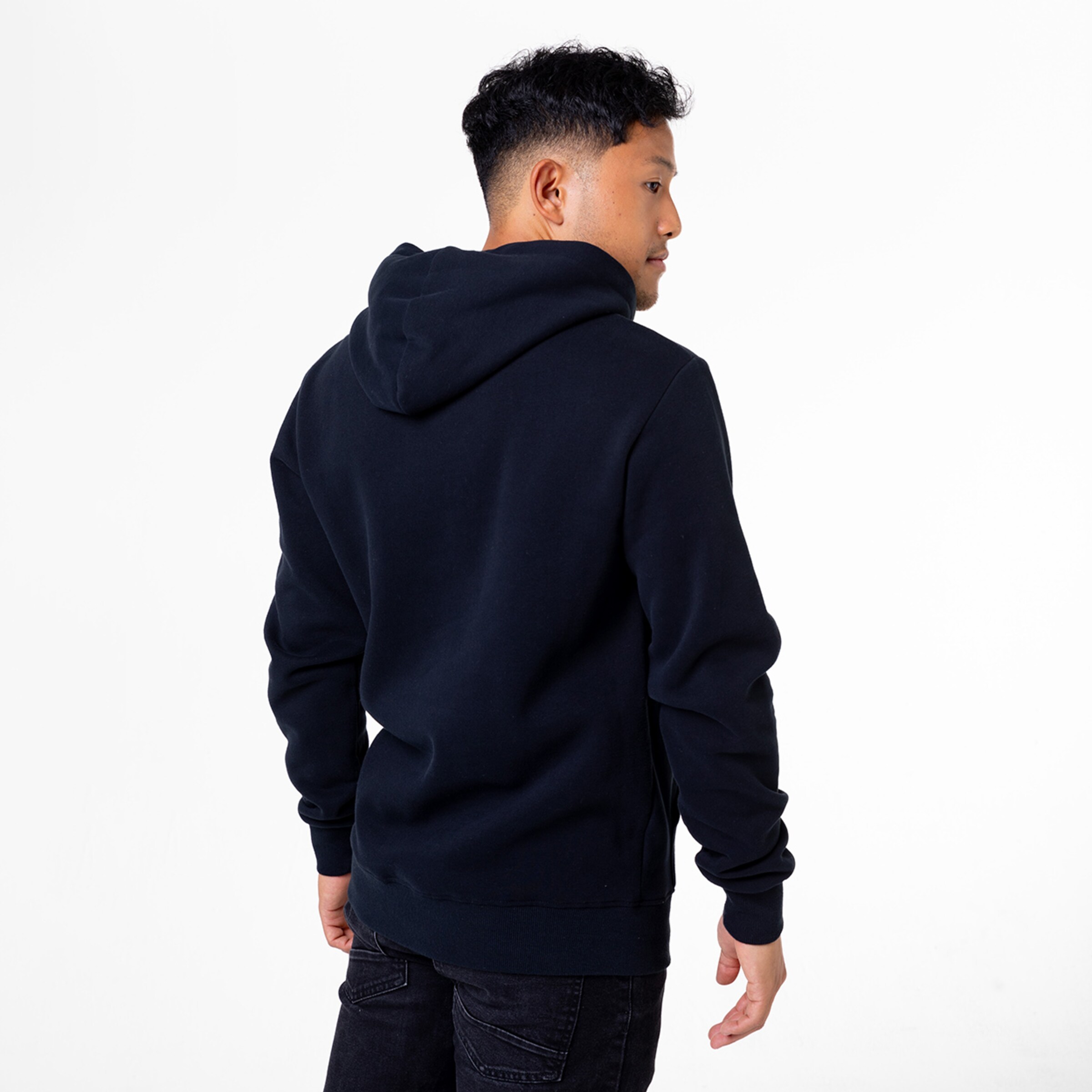 Junger Mann mit lockigem Haar trägt einen dunklen Kapuzenpullover von hinten gesehen.