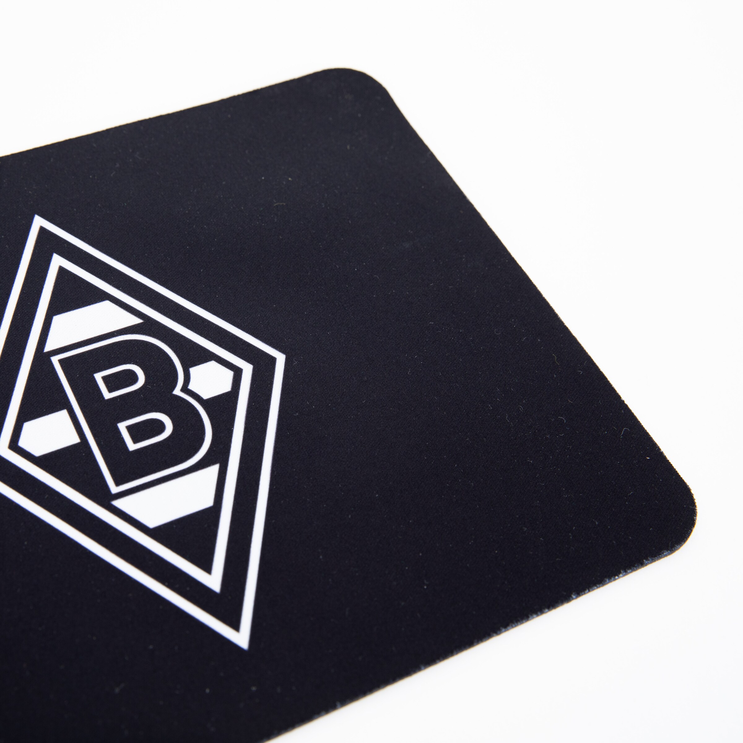 Ecke eines schwarzen Mauspads mit dem weißen Logo von Borussia Mönchengladbach (Raute mit B).