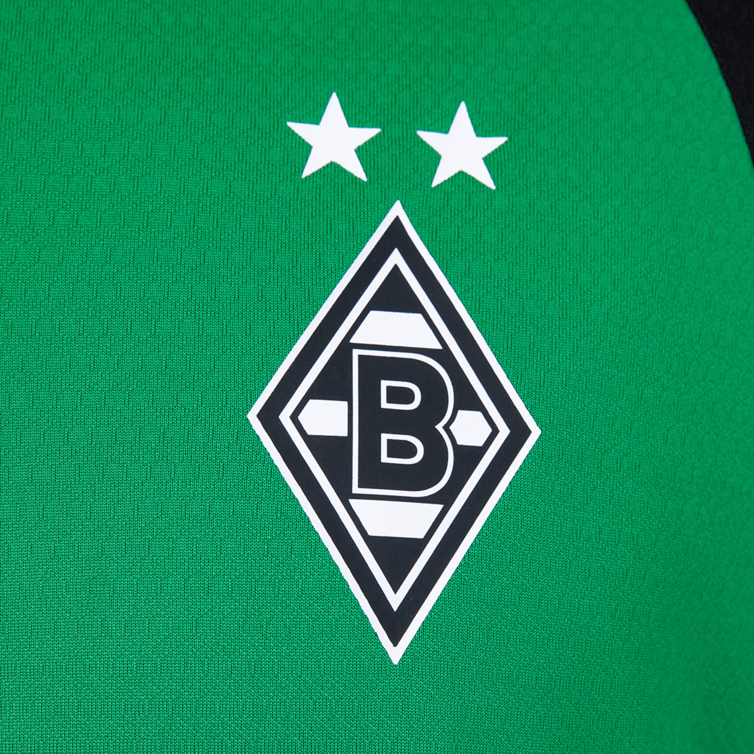 Nahaufnahme eines grünen Sporttrikots mit dem schwarz-weißen, rautenförmigen Logo von Borussia Mönchengladbach und zwei weißen Sternen darüber.