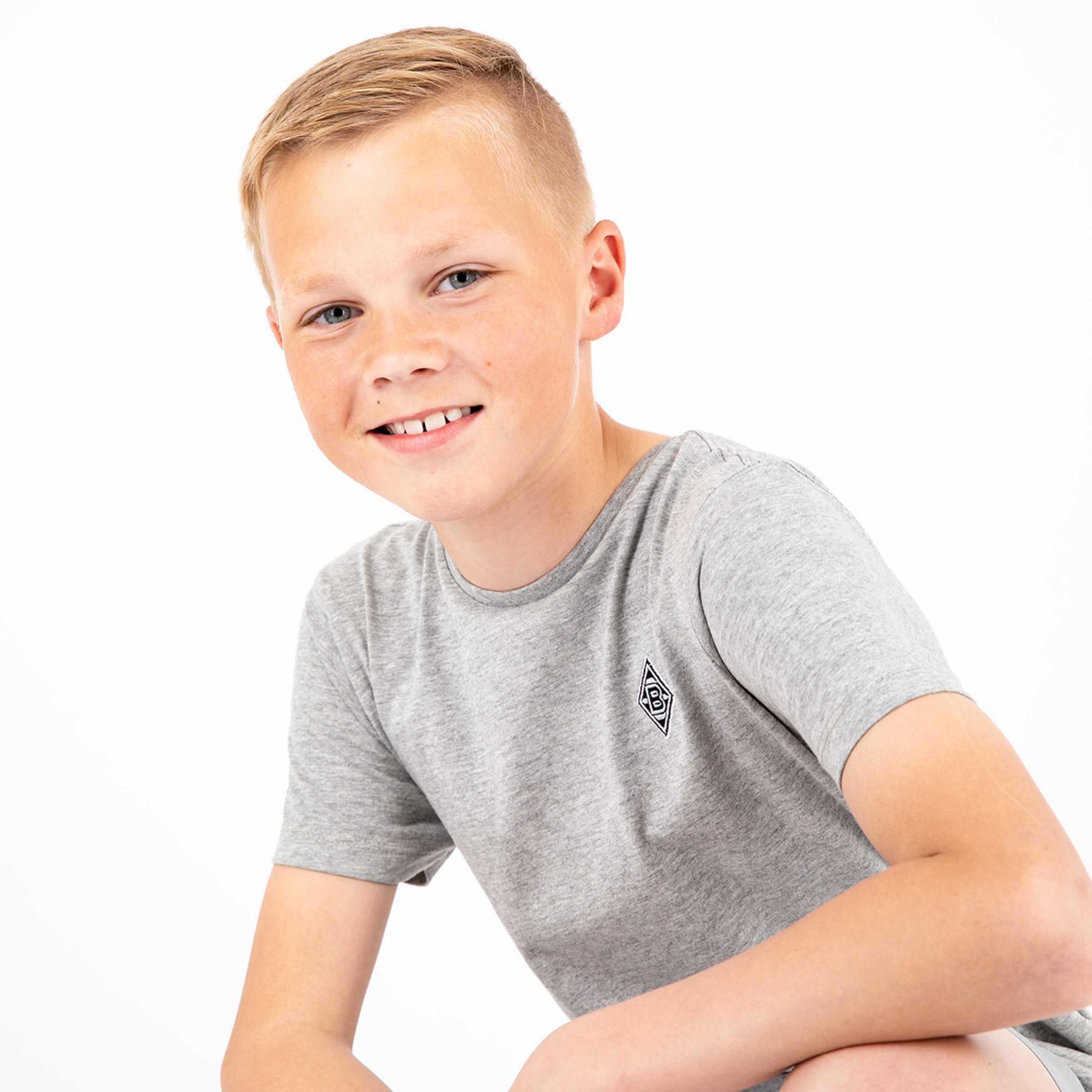Junge mit blondem Haar in grauem T-Shirt lächelt leicht.