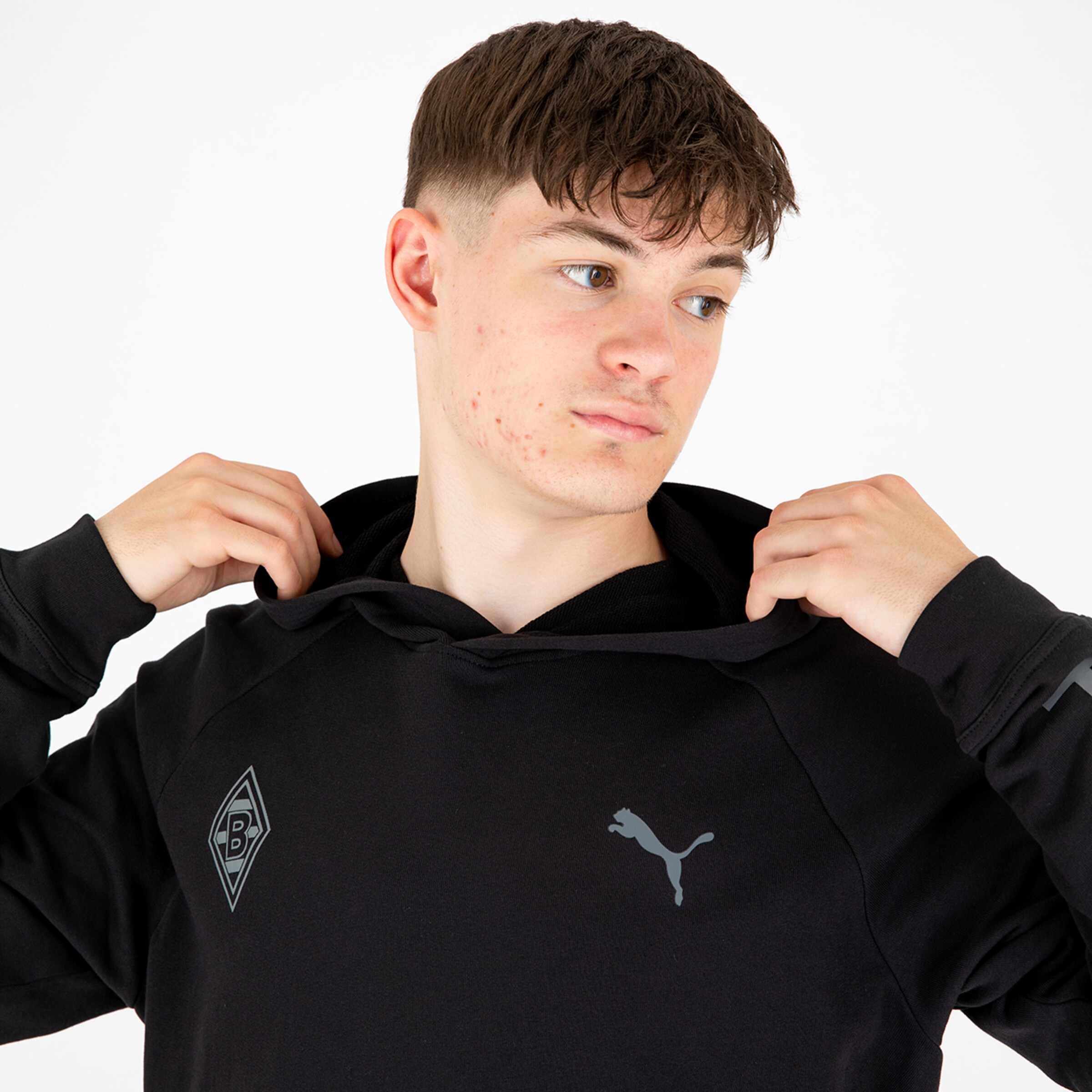 Junger Mann in schwarzem Hoodie mit Puma-Logo und Borussia Mönchengladbach-Wappen schaut über die Schulter.