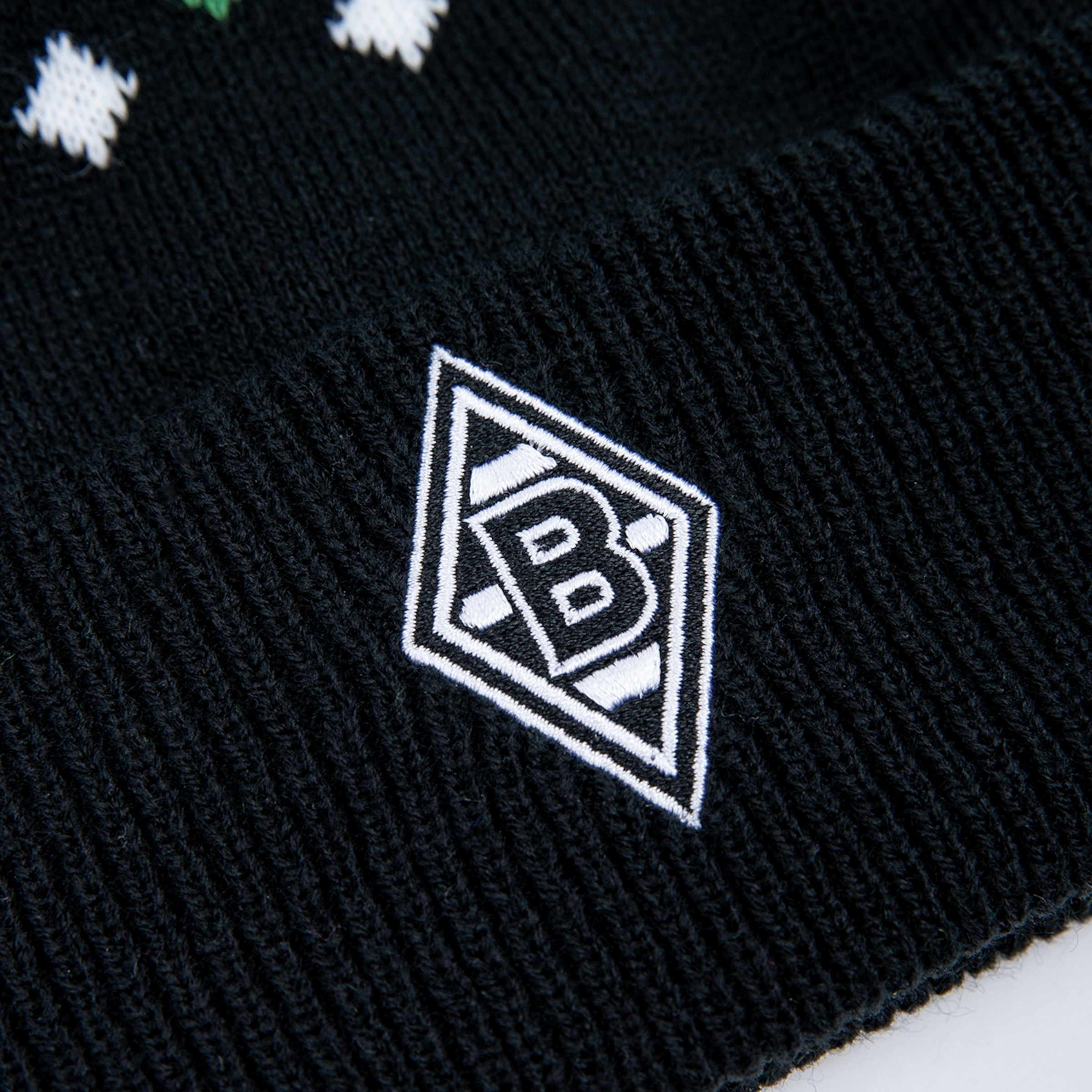 Close-up of a black knitted beanie with the white and black diamond logo of Borussia Mönchengladbach embroidered on the ribbed cuff.
