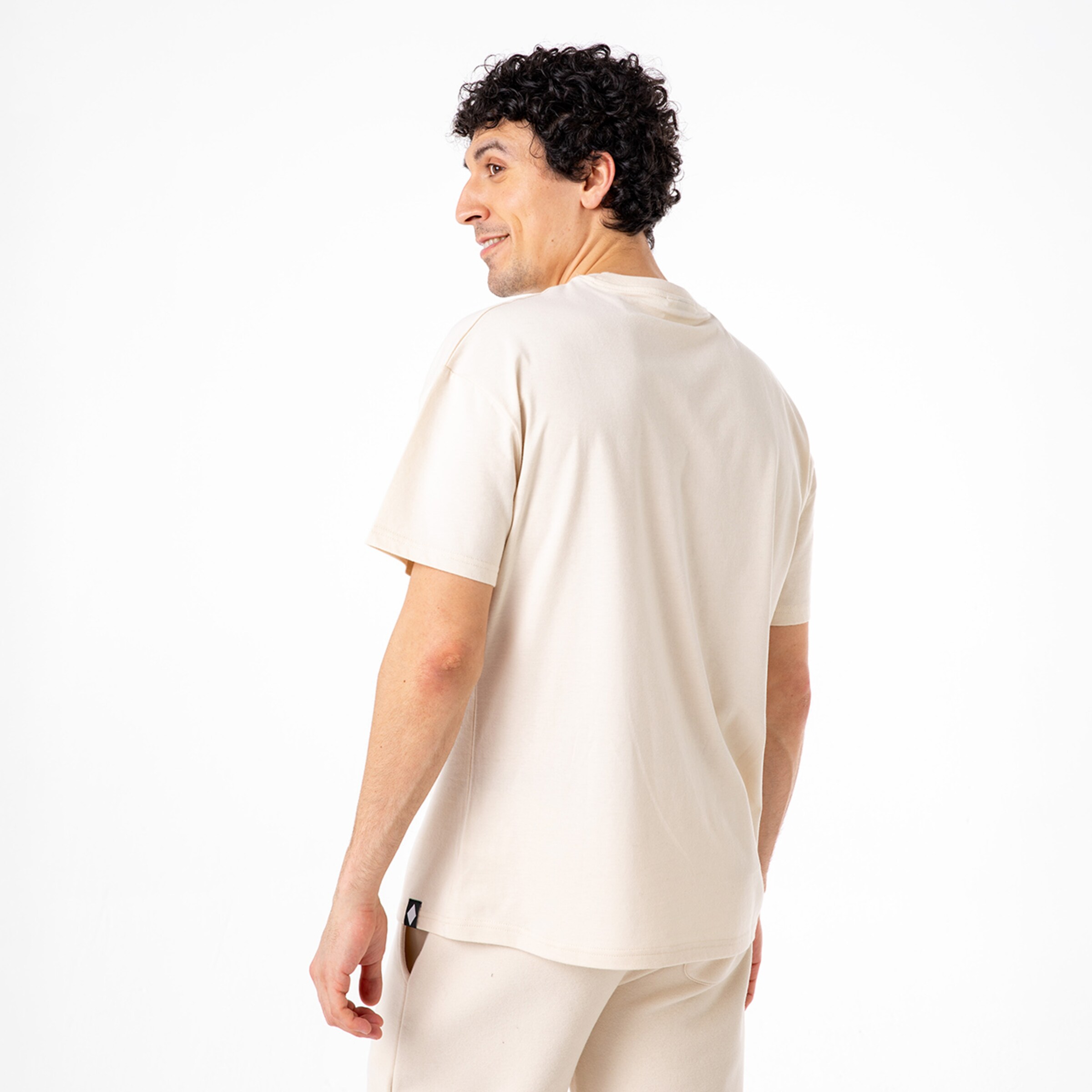 Mann mit lockigem Haar trägt ein helles T-Shirt und schaut über die Schulter zurück.