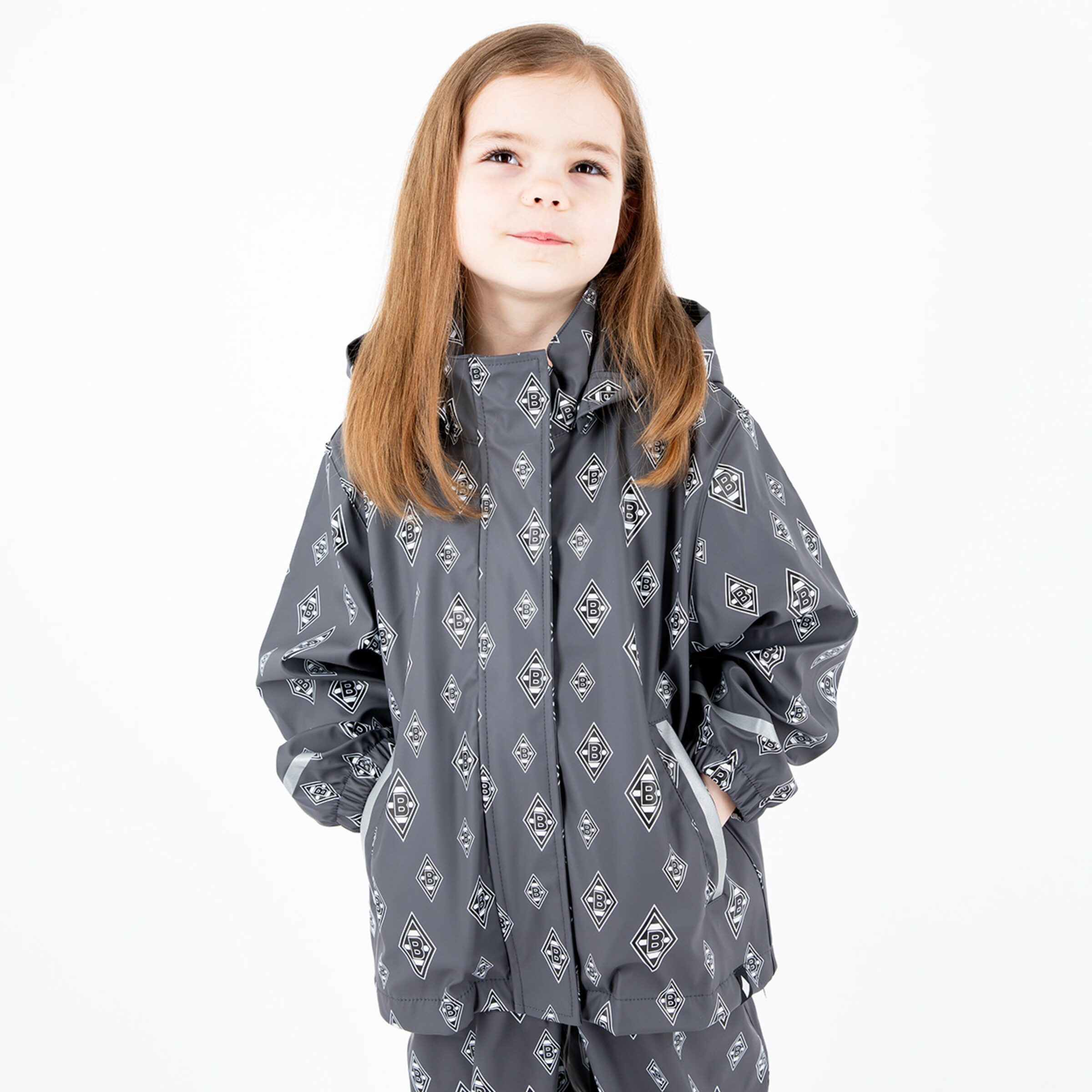 Ein Mädchen mit langen braunen Haaren trägt eine graue Regenjacke mit Muster.