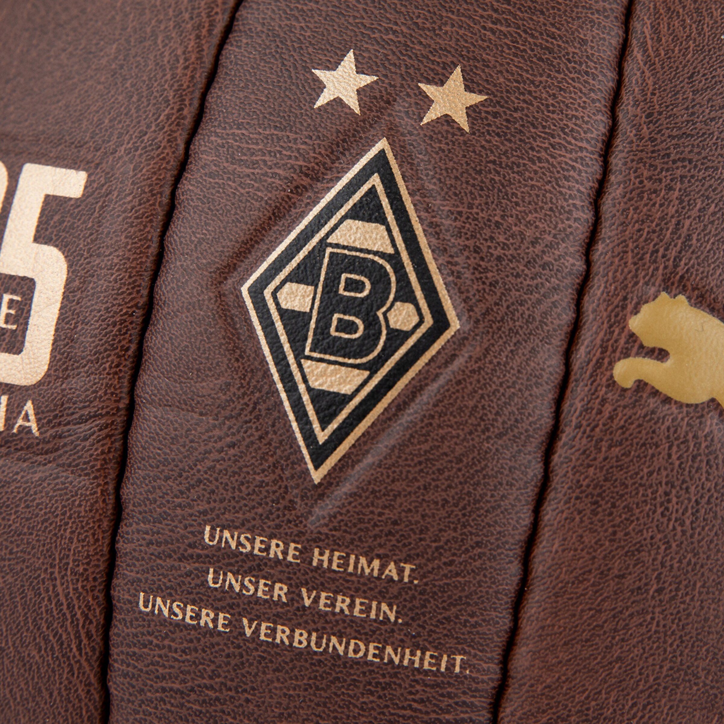 Detail eines braunen Lederfußballs mit goldenem Borussia Mönchengladbach Logo, Sternen und dem Motto: UNSERE HEIMAT. UNSER VEREIN.