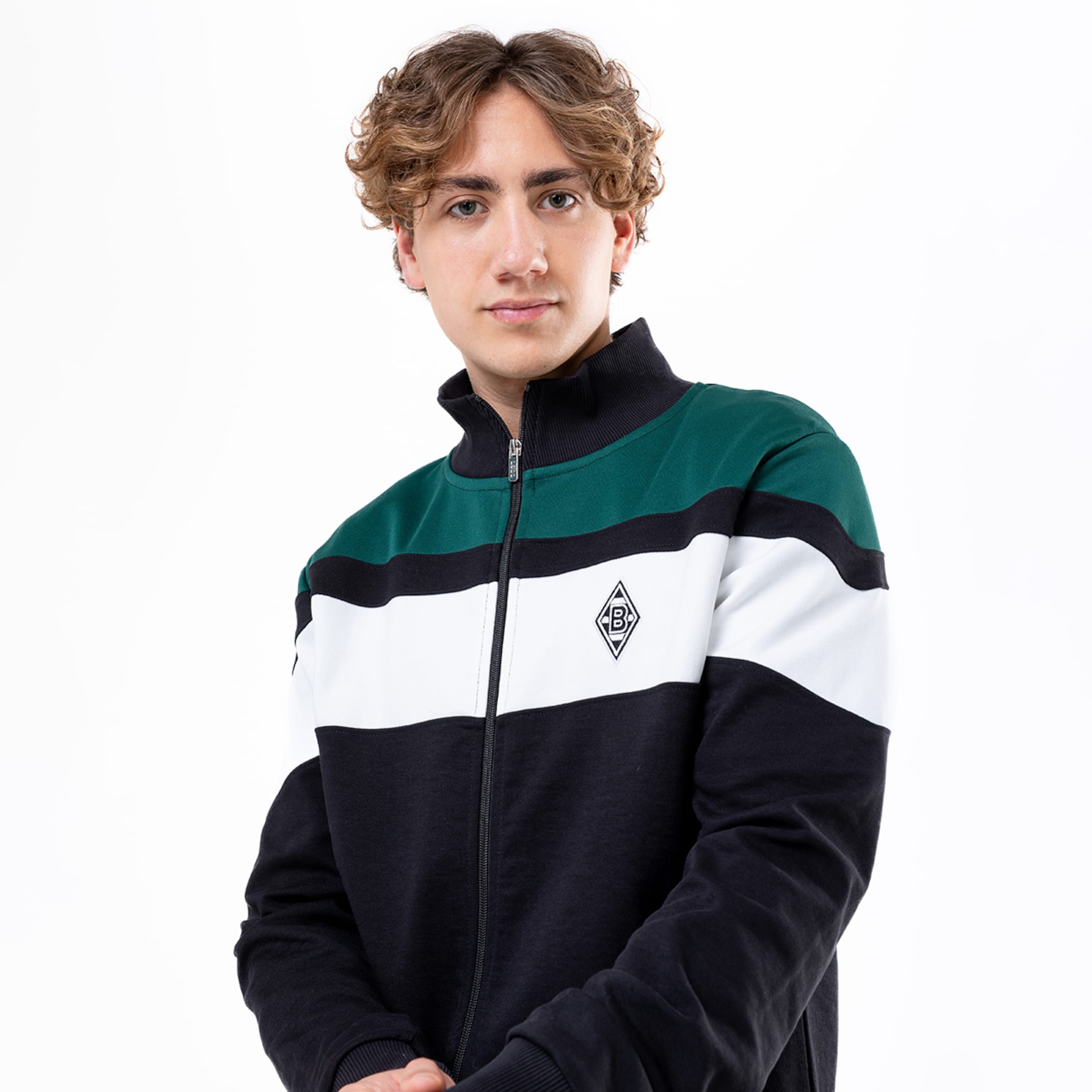 Junger Mann mit lockigen Haaren in einer Farbblock-Jacke von Borussia Mönchengladbach.