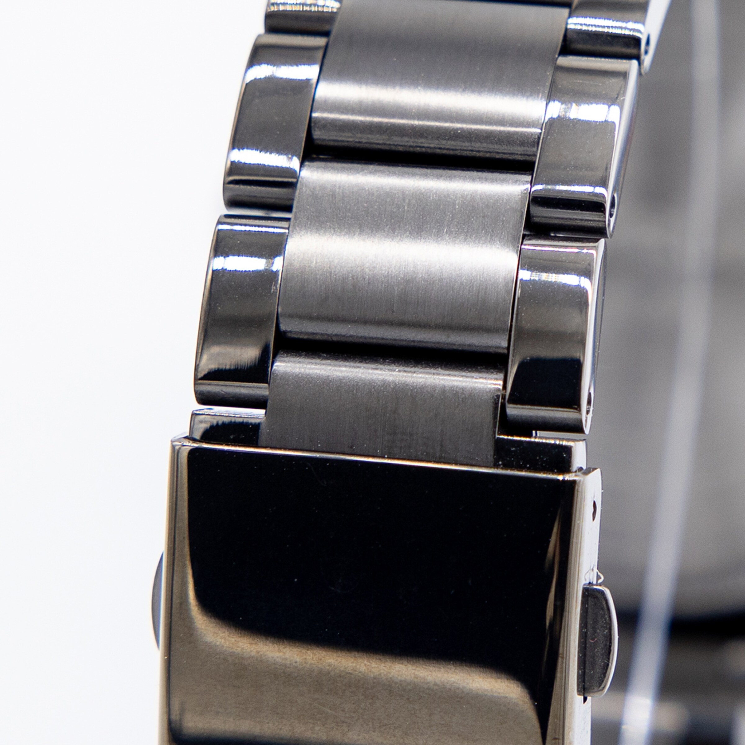 Detail eines schwarzen Metall-Uhrenarmbands mit gebürsteten Gliedern und glänzender Schließe vor weißem Hintergrund.