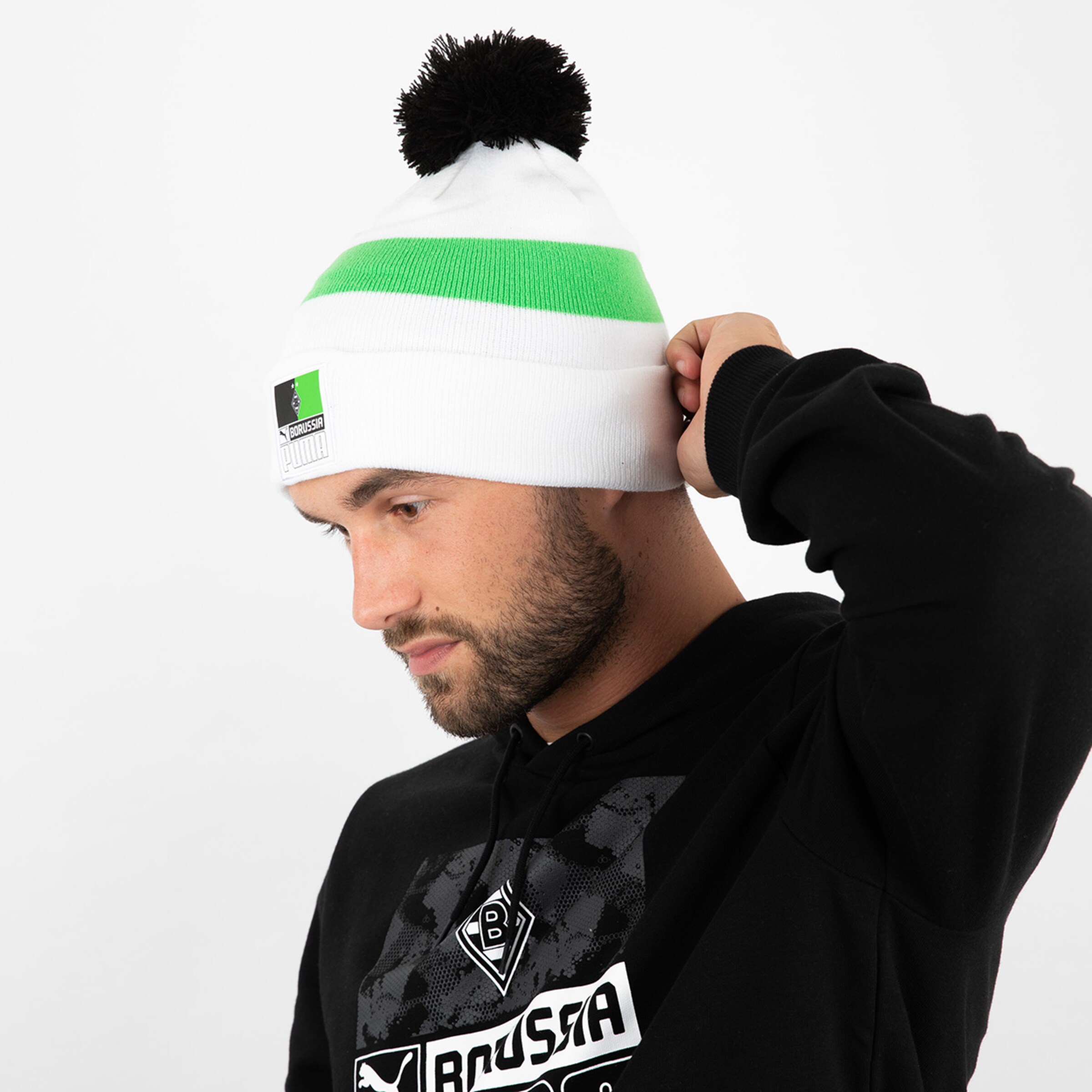 Mann trägt eine weiße Mütze mit grünen Streifen und Bommel schaut nach unten.