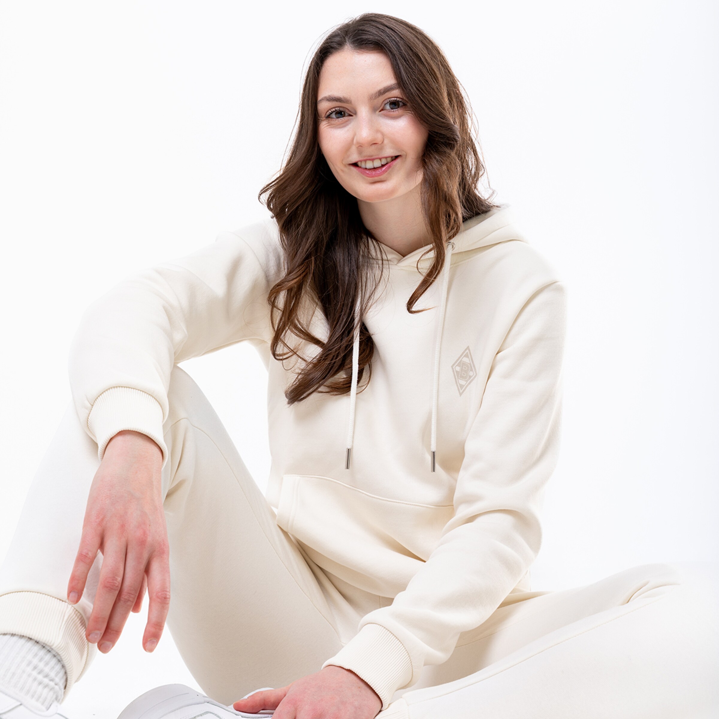 Eine Frau sitzt lächelnd in einem beigen Hoodie und Jogginghose.