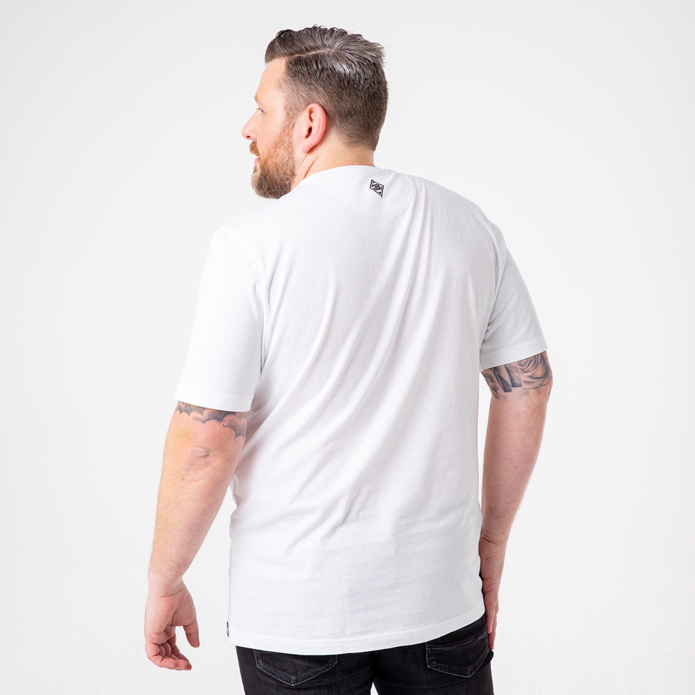 Mann mit tätowierten Armen trägt ein weißes T-Shirt Rückansicht.