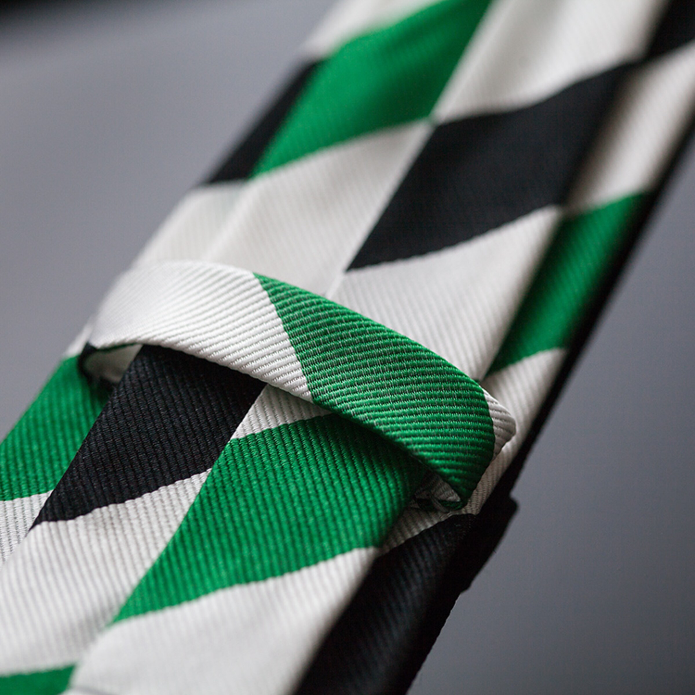 Grün-schwarz-weiße Krawatte mit Rautenmuster gefaltet und auf einer glatten Oberfläche.