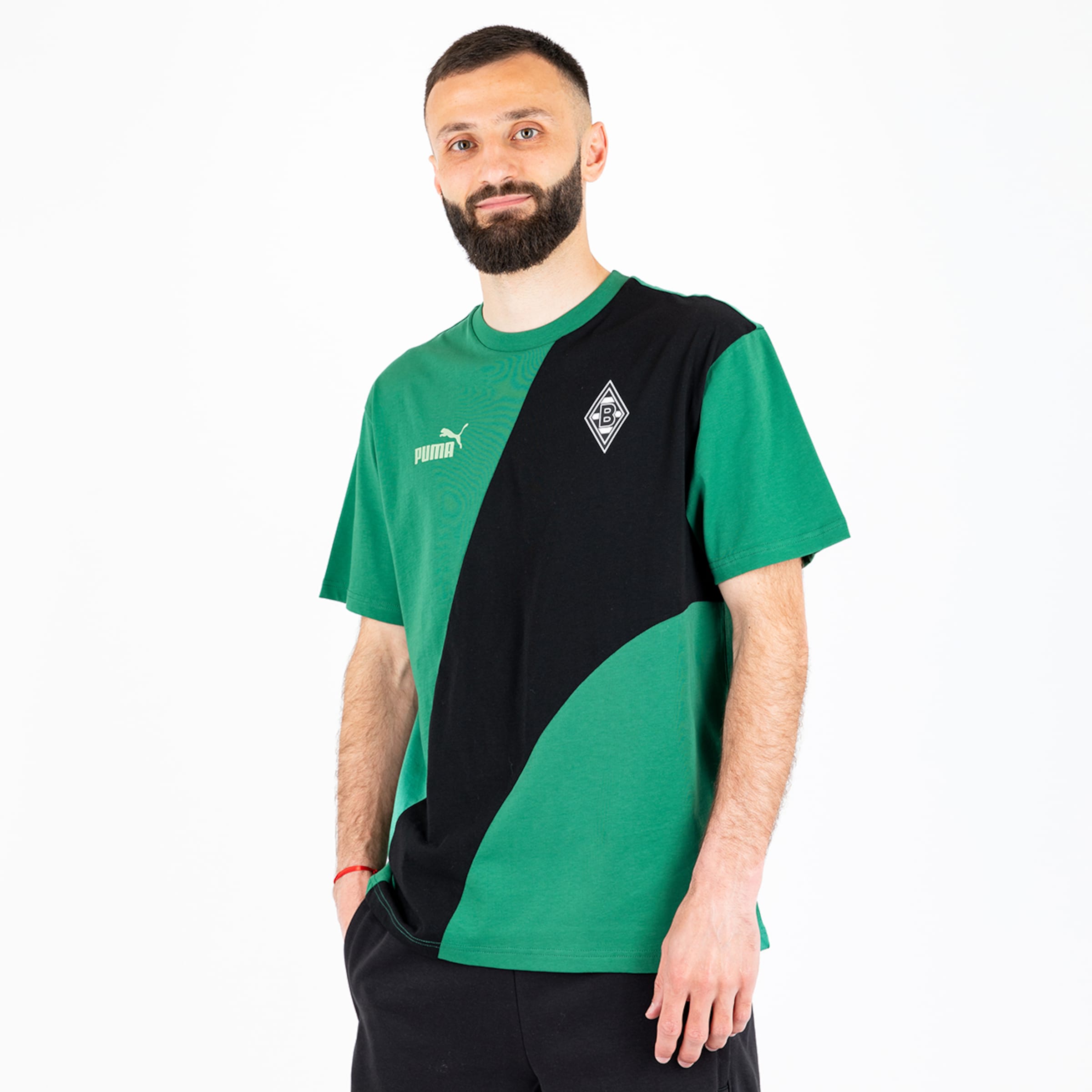 Ein männlicher Modell trägt ein grünes T-Shirt mit schwarzem Designelement und dem Borussia Mönchengladbach-Logo.