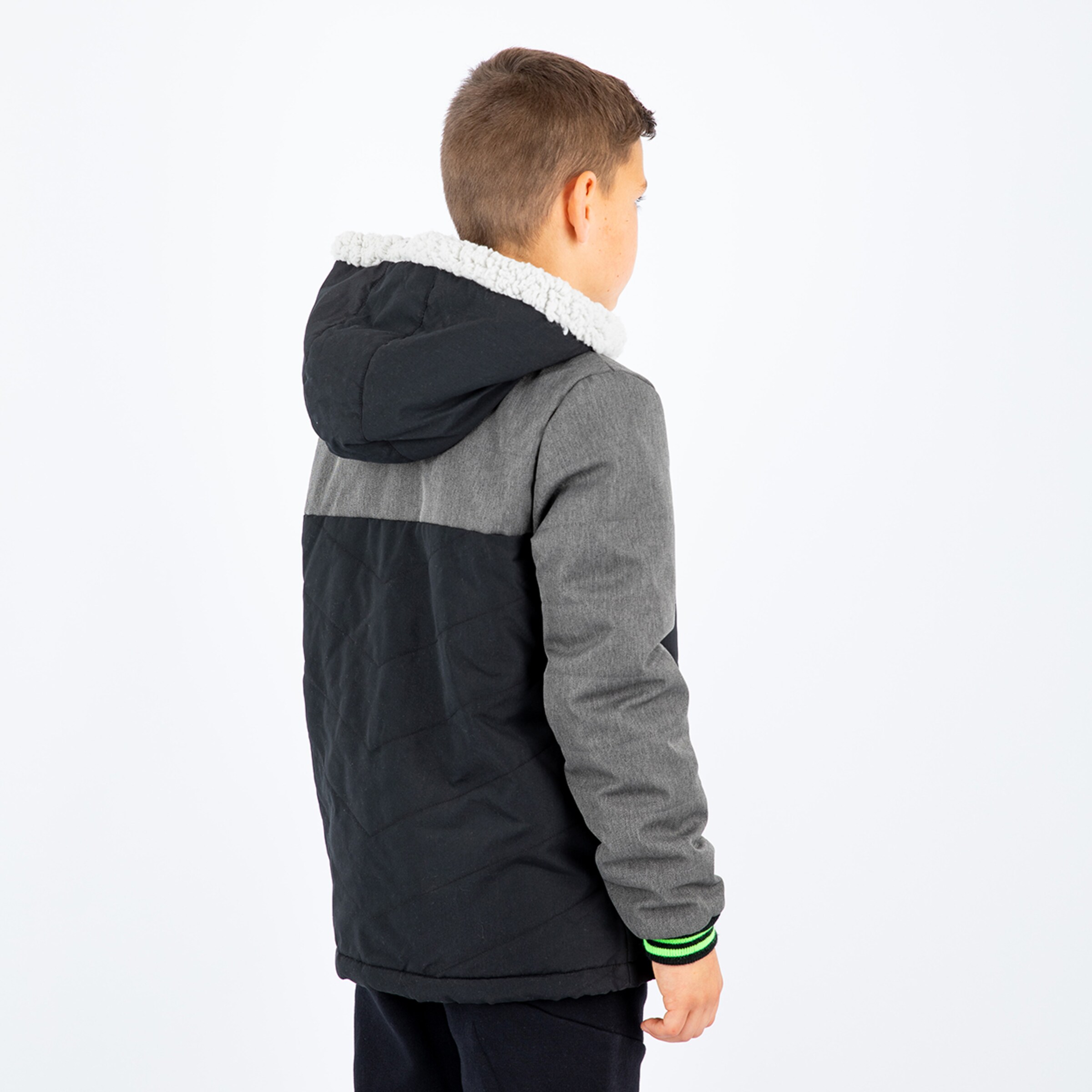Boy standing from behind in a black and gray jacket with a hood.