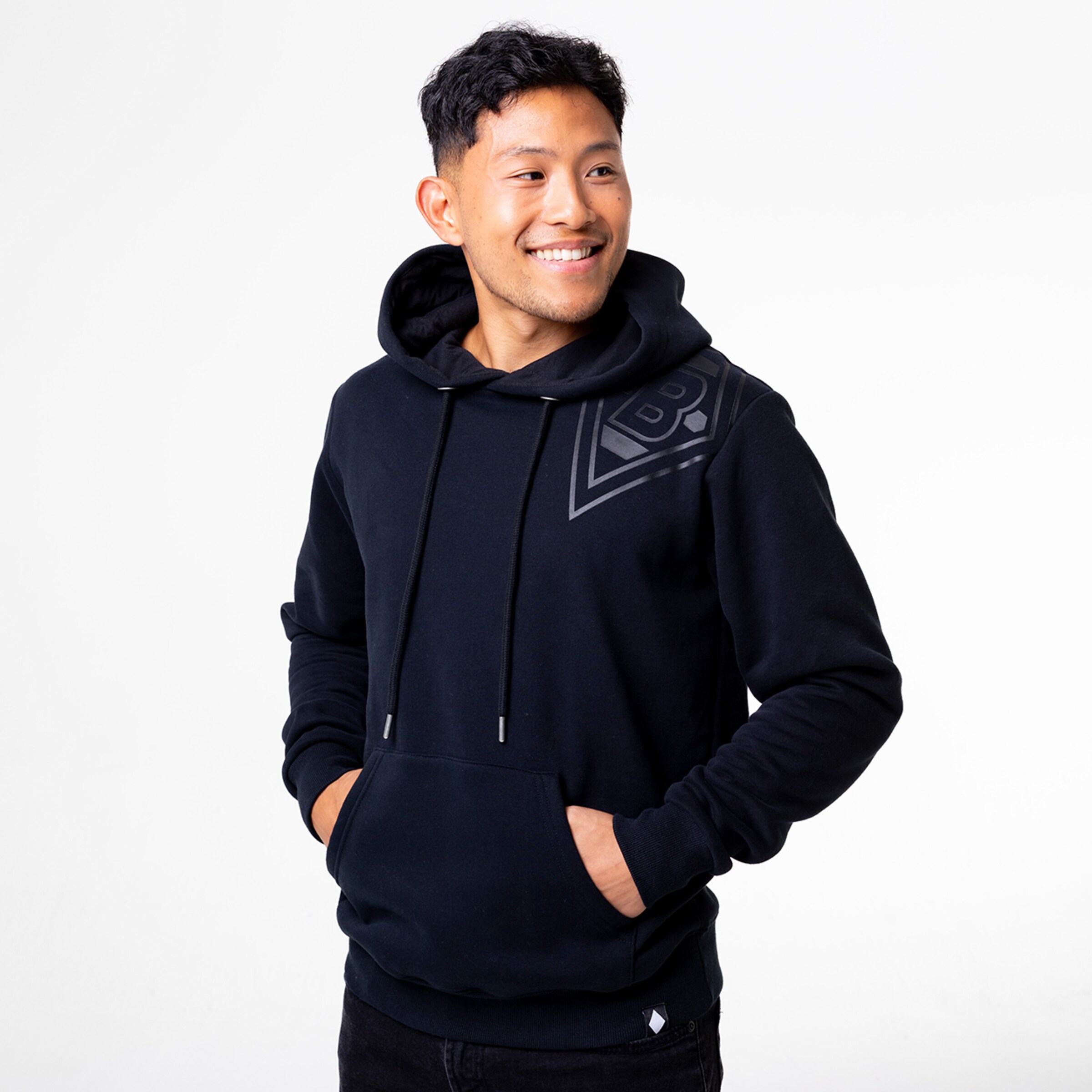 Mann trägt schwarzen Hoodie mit Kapuze und lächelt Hände in der Tasche.