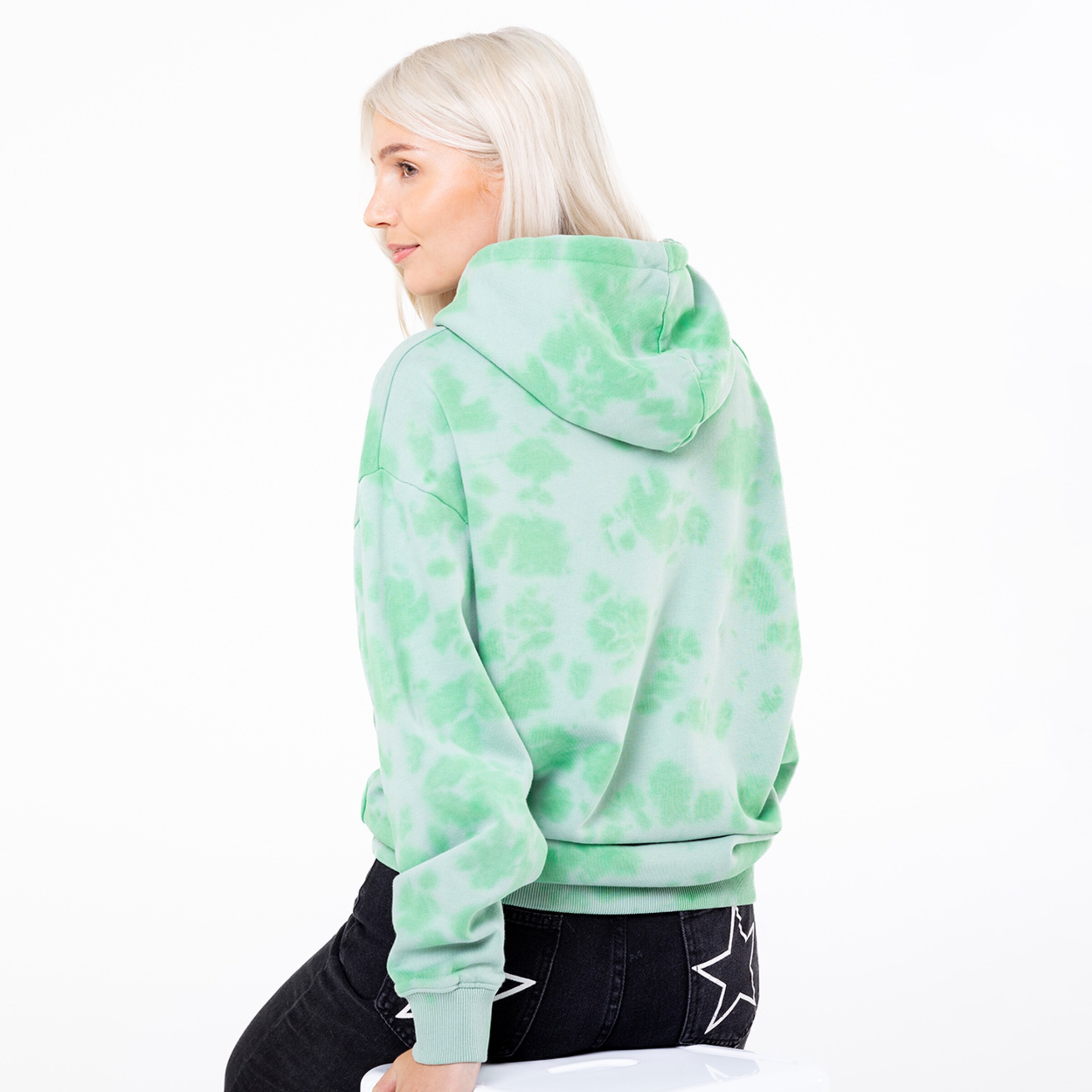 Woman with blonde hair wearing a green tie-dye hoodie viewed from behind.