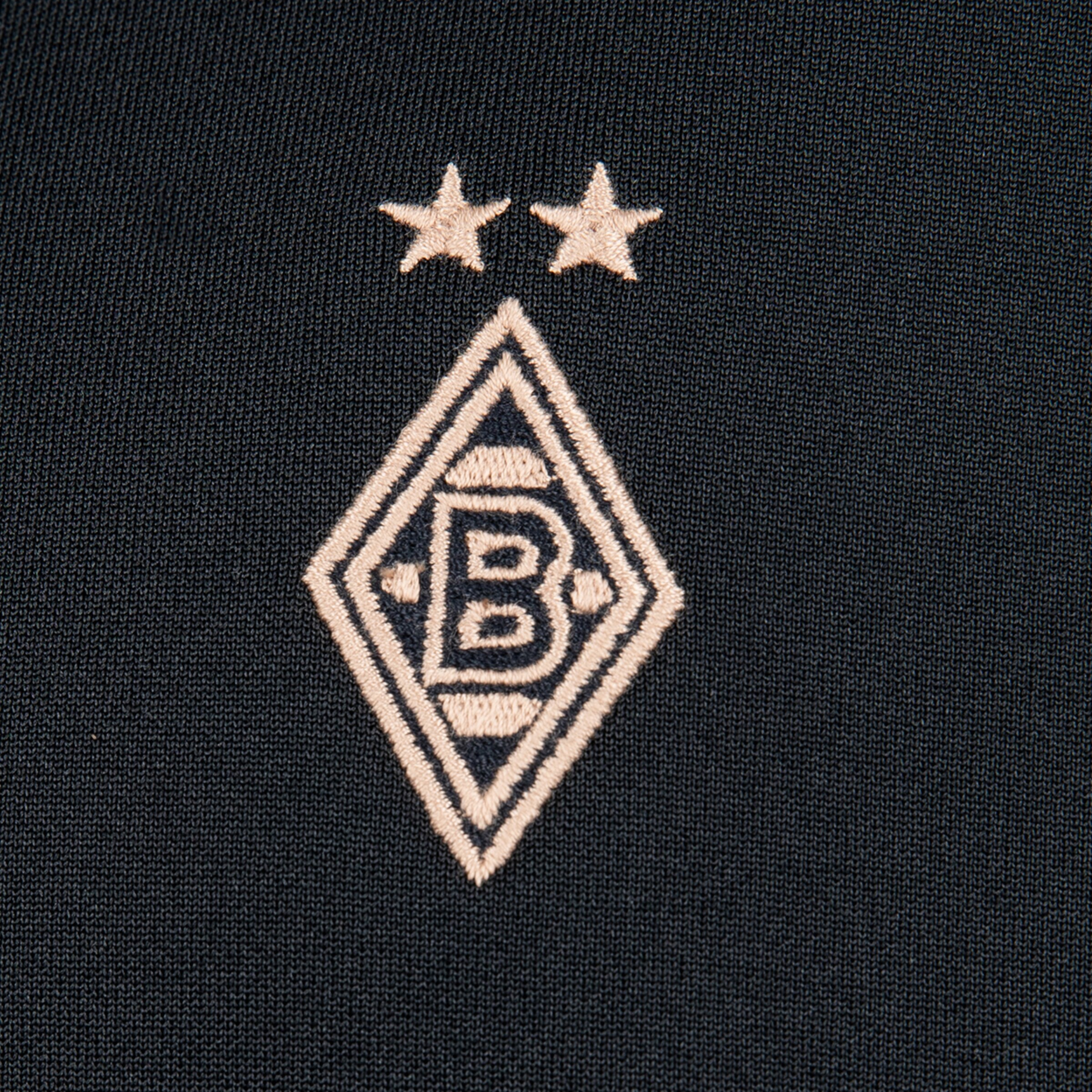 Gesticktes Logo von Borussia Mönchengladbach auf dunklem Stoff: Eine Raute mit dem Buchstaben B und zwei Sternen darüber.