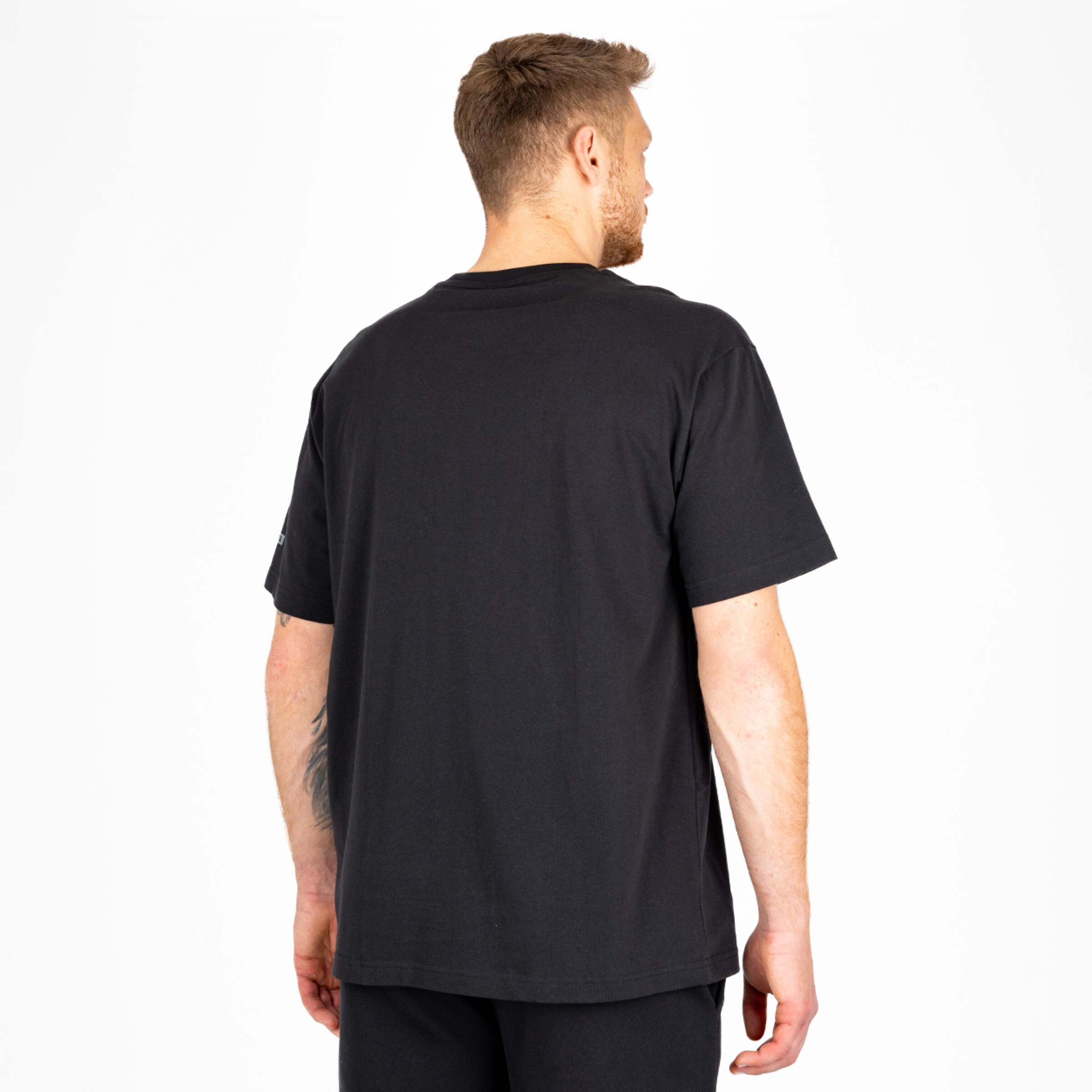 Man wearing a plain black t-shirt photographed from the back in a neutral stance.