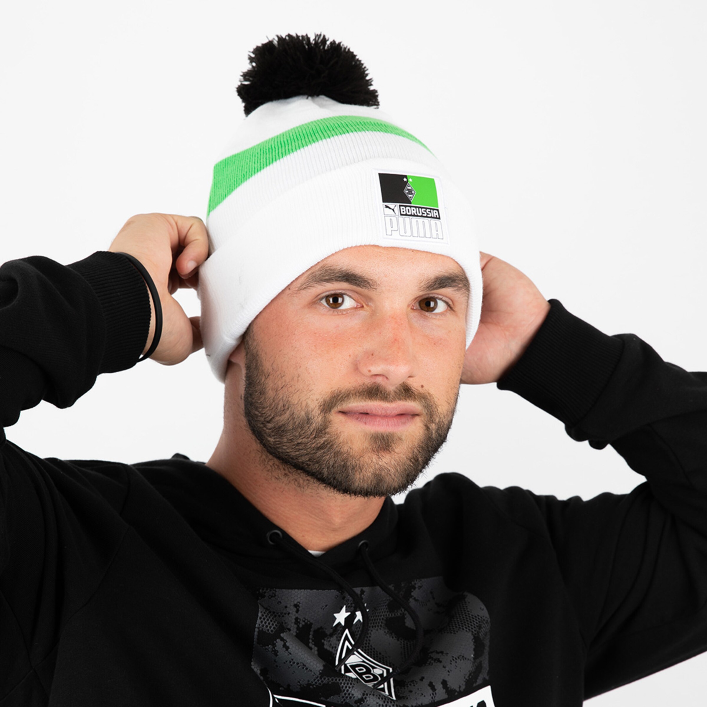 Mann mit Mütze und schwarzem Hoodie hält die Mütze am Kopf.