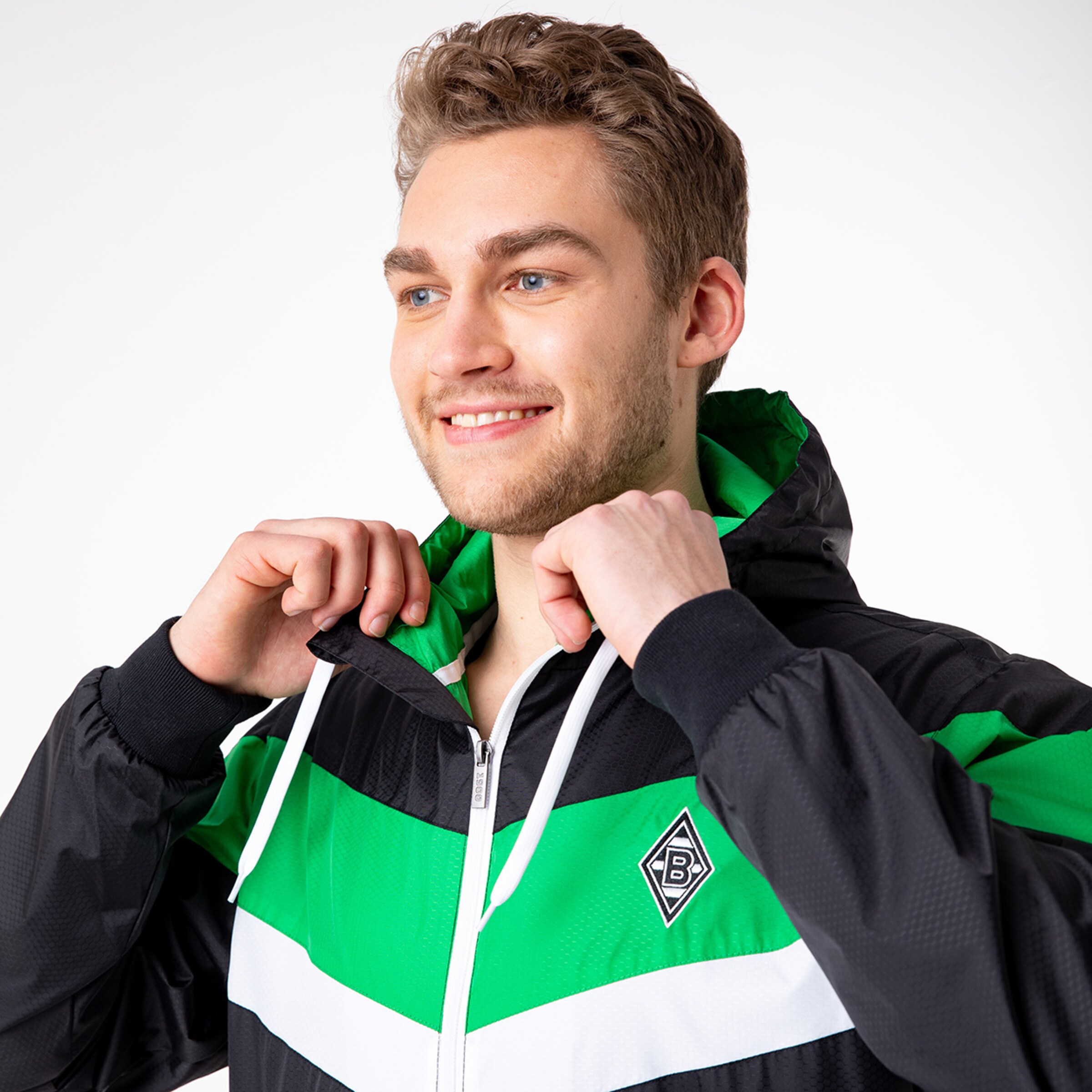 Ein junger Mann in einer schwarz-grünen Jacke mit einem lächelnden Gesichtsausdruck.