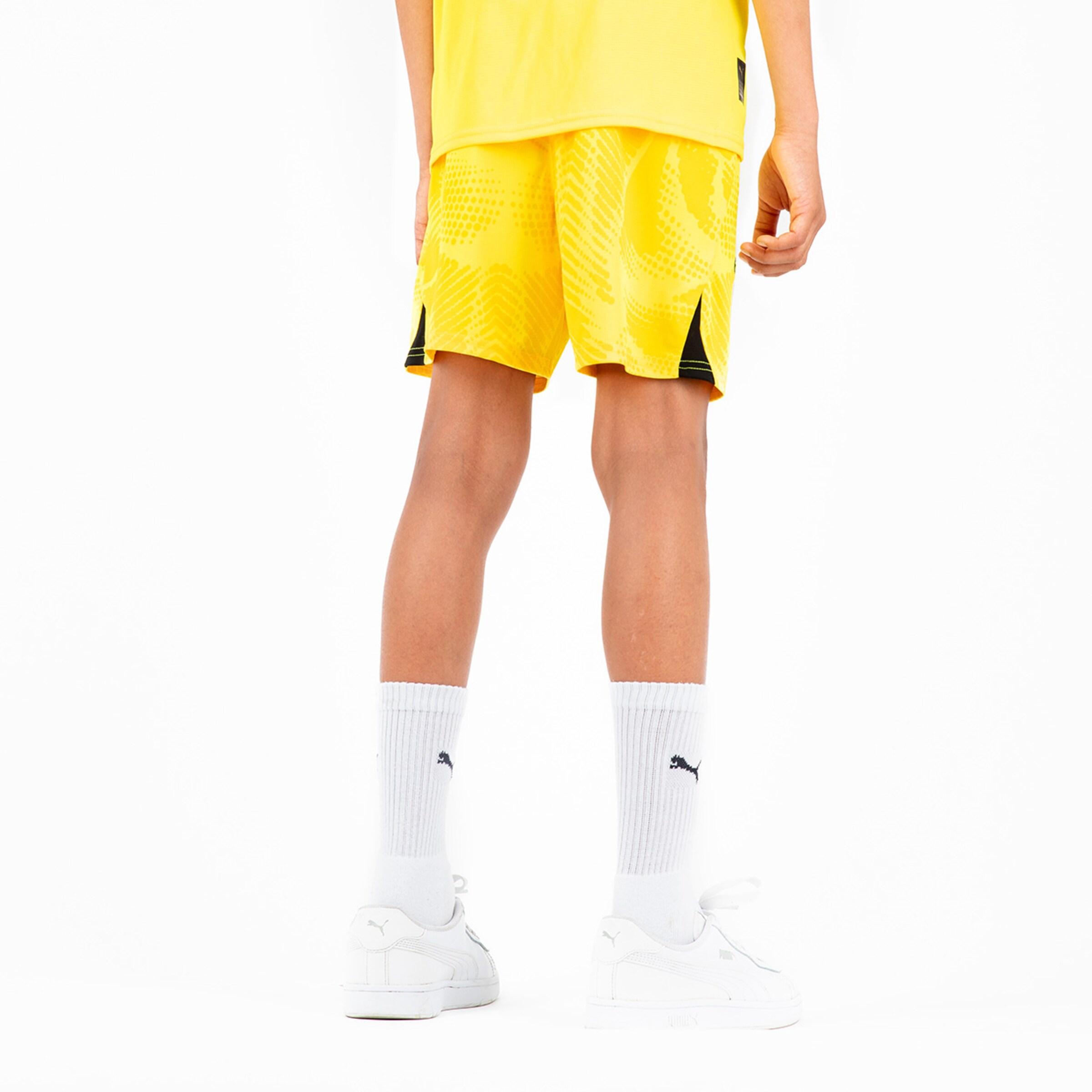 Junge trägt gelbe Sportshorts und weiße Socken mit Puma-Logo.