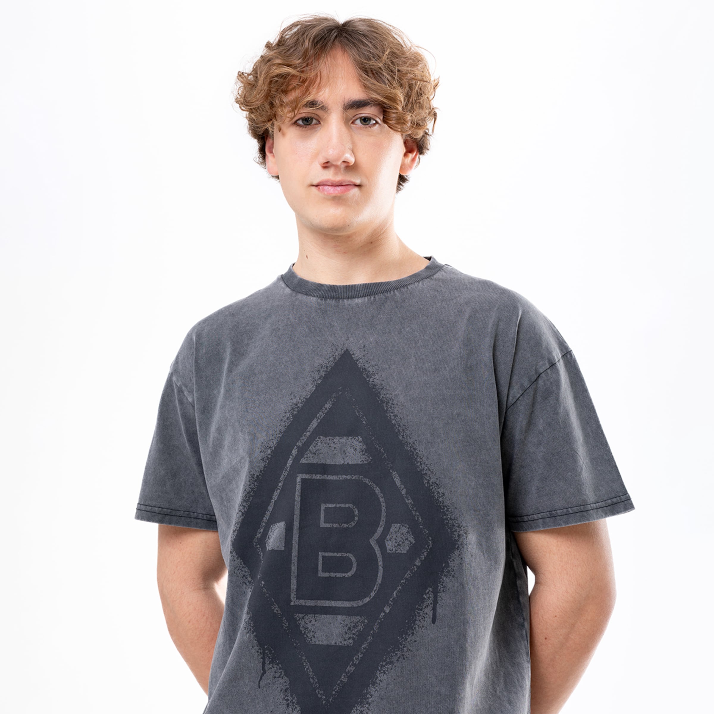 Mann mit lockigem Haar trägt ein graues T-Shirt mit Borussia Mönchengladbach-Logo.