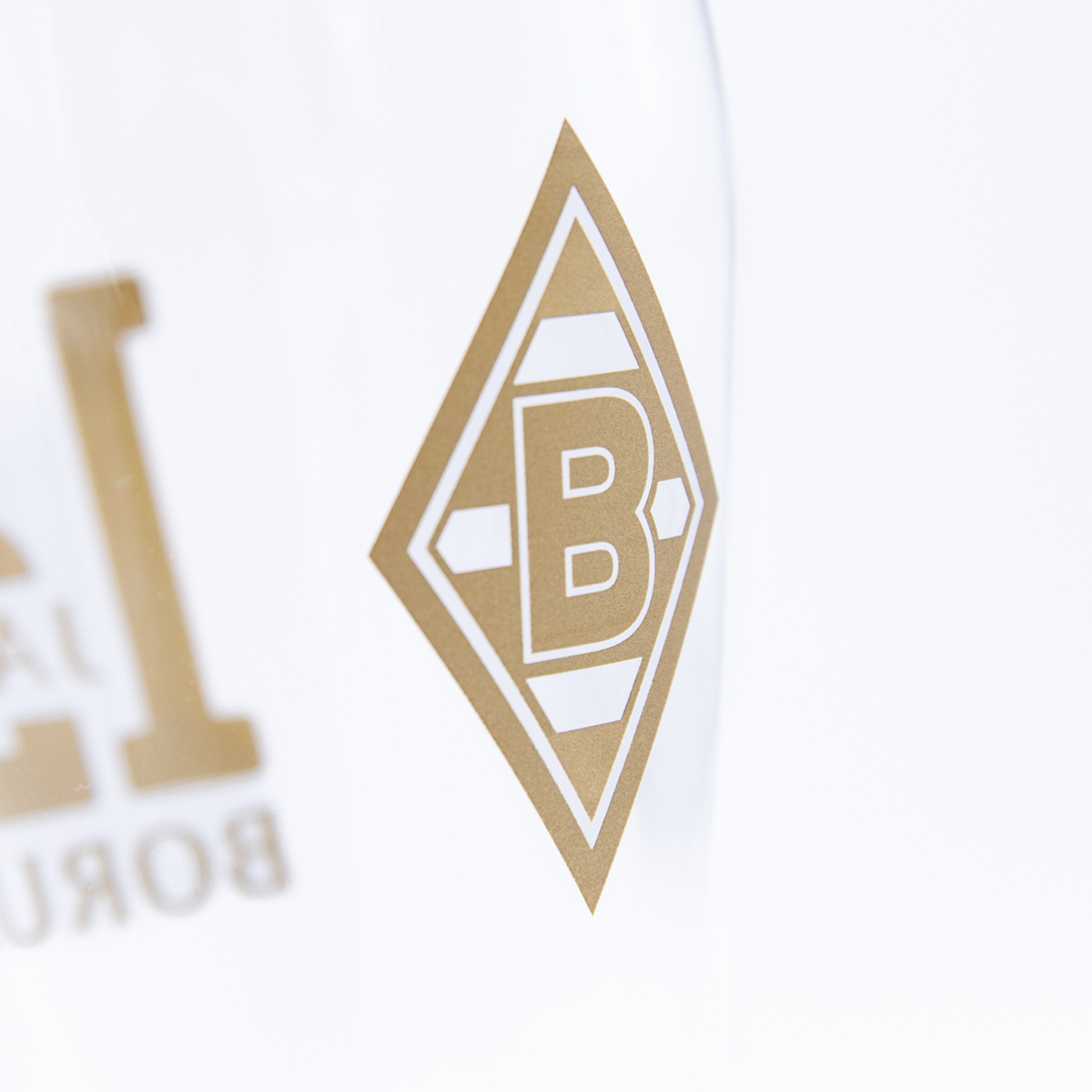 Nahaufnahme des goldenen Borussia Mönchengladbach Logos (Raute mit 'B') auf transparentem Grund.