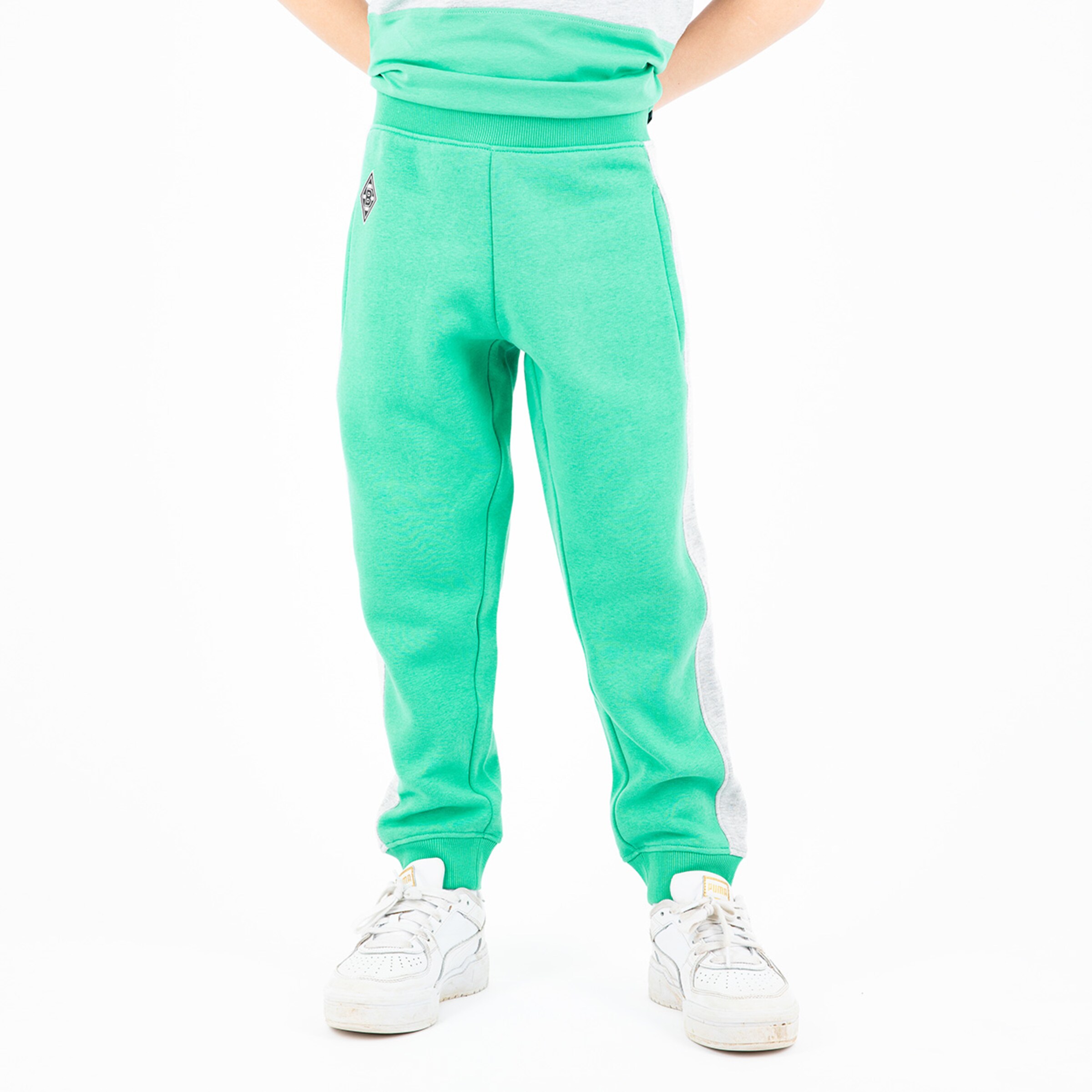 Grüne Jogginghose für Kinder mit grauen Seiteneinsätzen kombiniert mit weißen Turnschuhen.