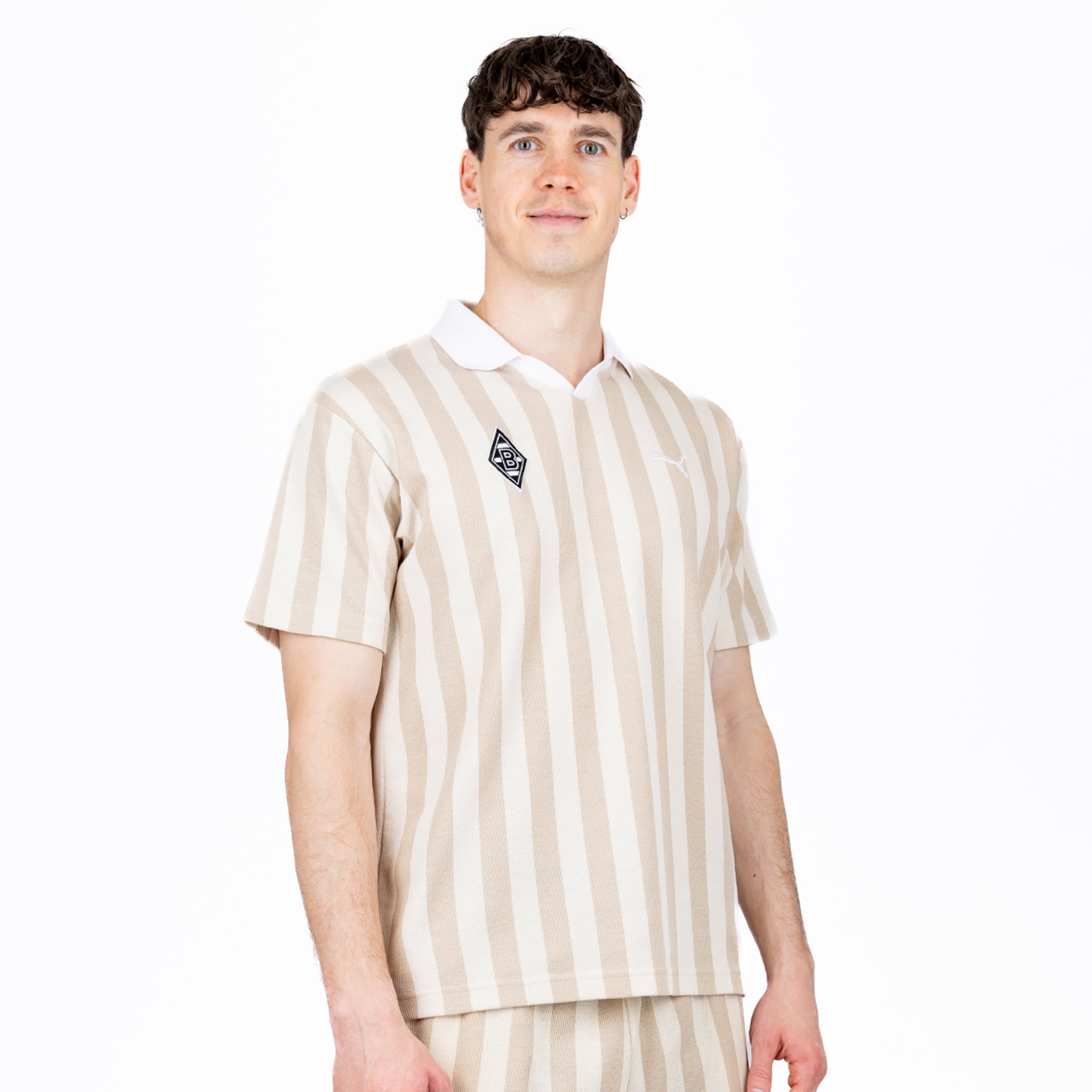 Junger Mann in beige-weiß gestreiftem Poloshirt und passenden Shorts mit Borussia Mönchengladbach-Logo vor weißem Hintergrund.