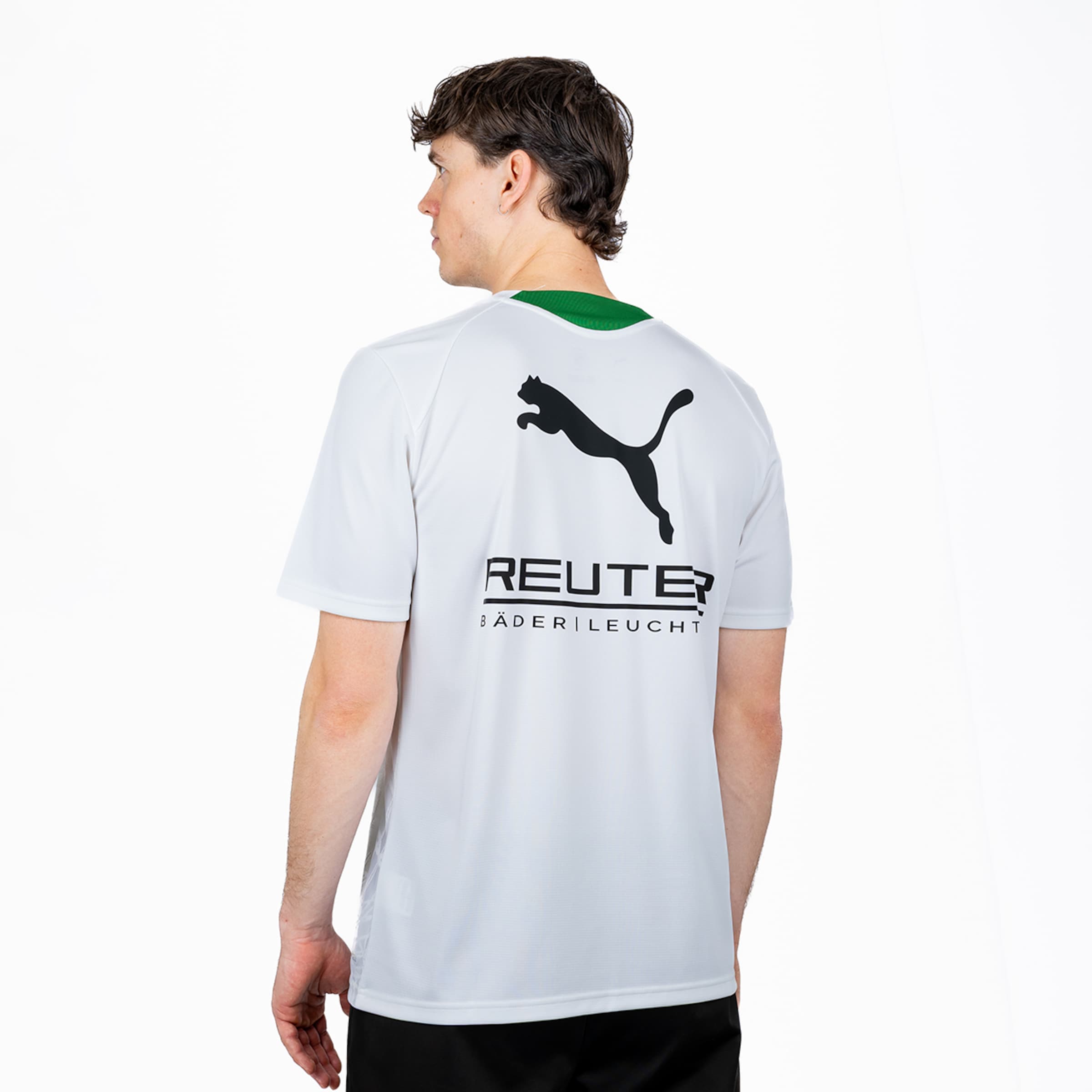 Ein Mann, von hinten und leicht nach links gedreht, trägt ein weißes T-Shirt mit grünem Kragen. Auf dem Rücken des Shirts sind ein großes schwarzes Puma-Logo und darunter der Schriftzug "REUTER" mit "BÄDER|LEUCHT" zu sehen.