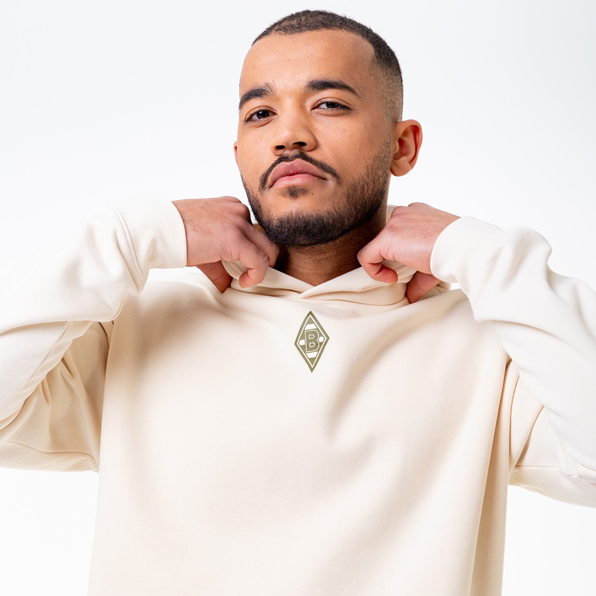 Mann mit kurzrasiertem Bart trägt ein helles Kapuzenshirt mit dem Borussia Mönchengladbach-Logo.