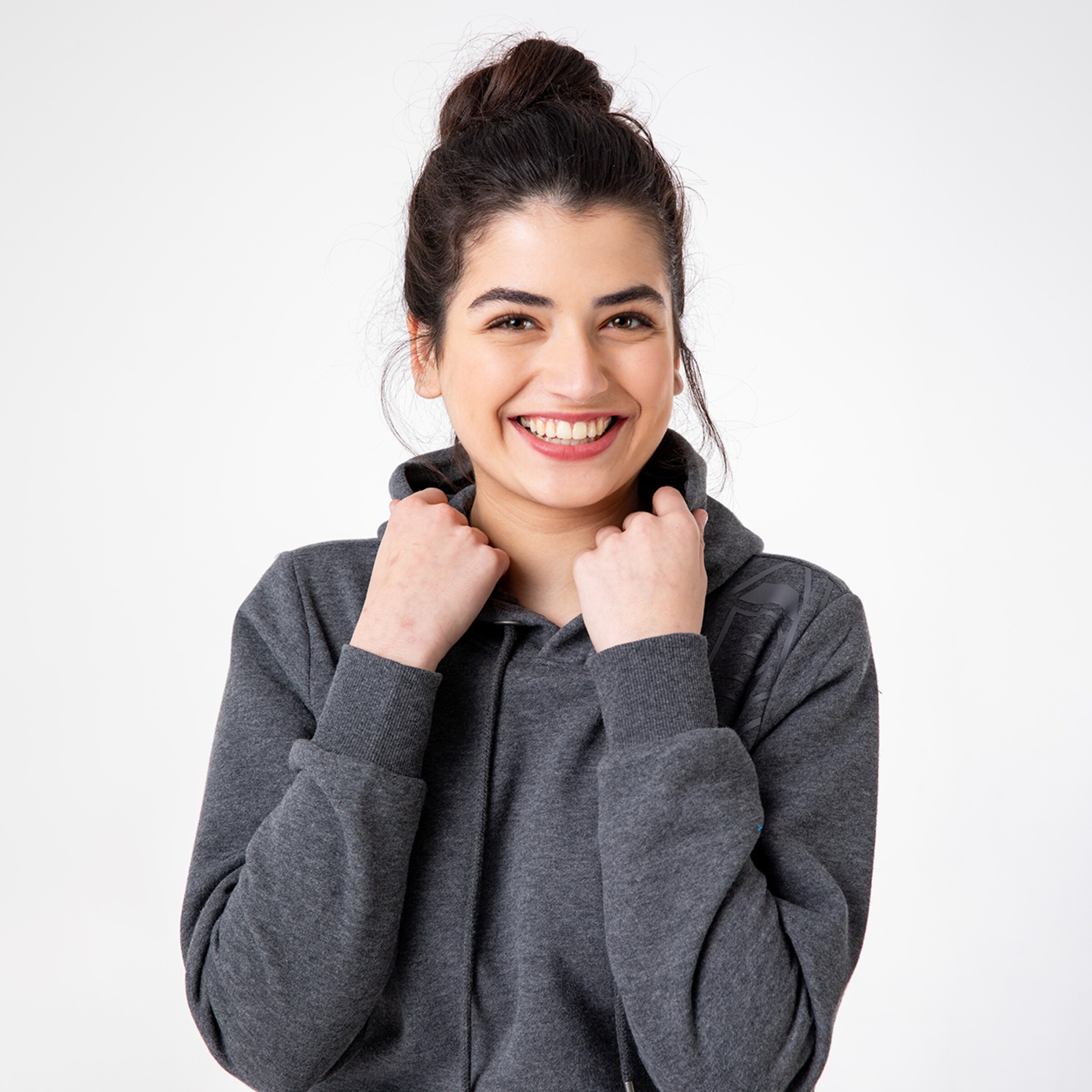 Junge Frau mit dunklen Haaren in grauer Hoodie lächelt freundlich.