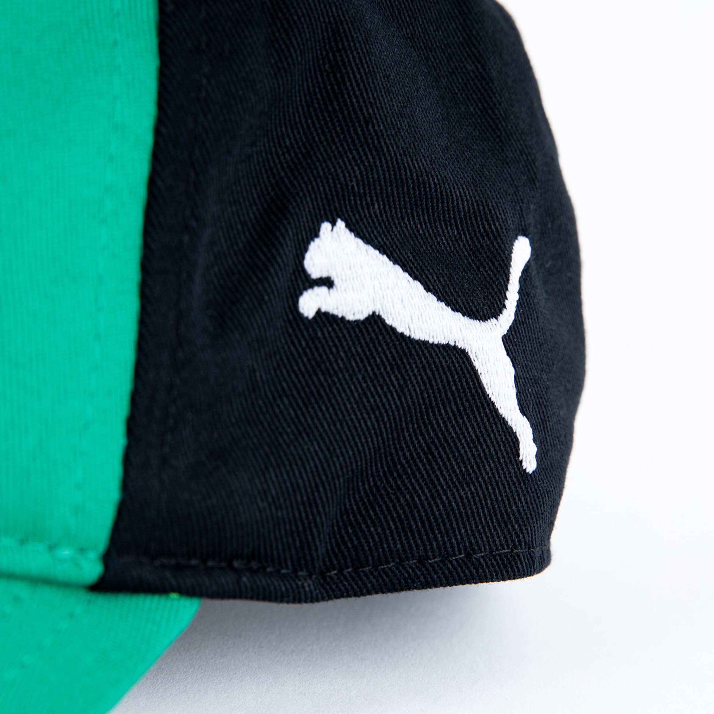 Detailansicht eines PUMA-Logos auf einer schwarzen Kappe mit grünen Akzenten.