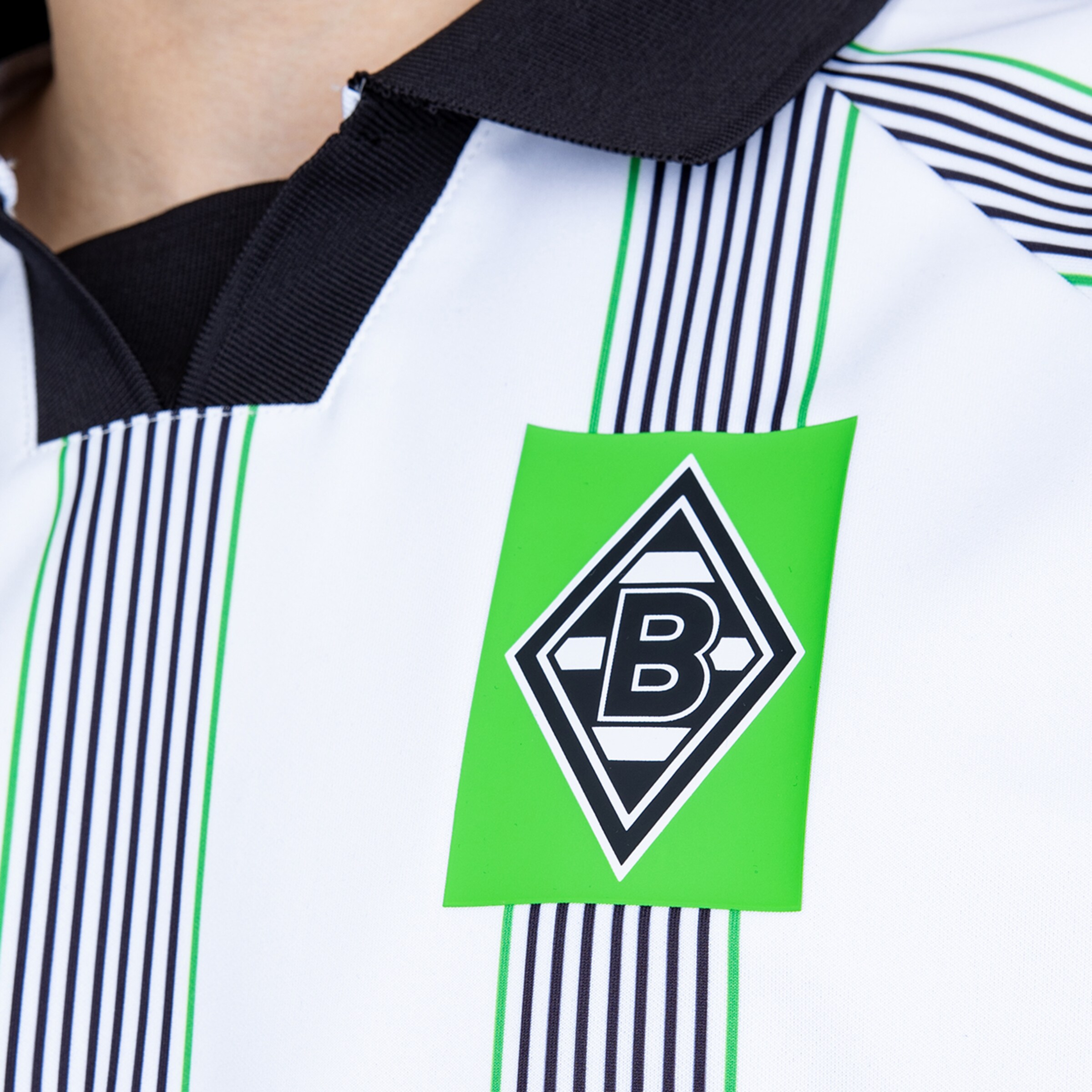 Close-up of a Borussia Mönchengladbach soccer jersey with the club logo on white fabric featuring green and black stripes.