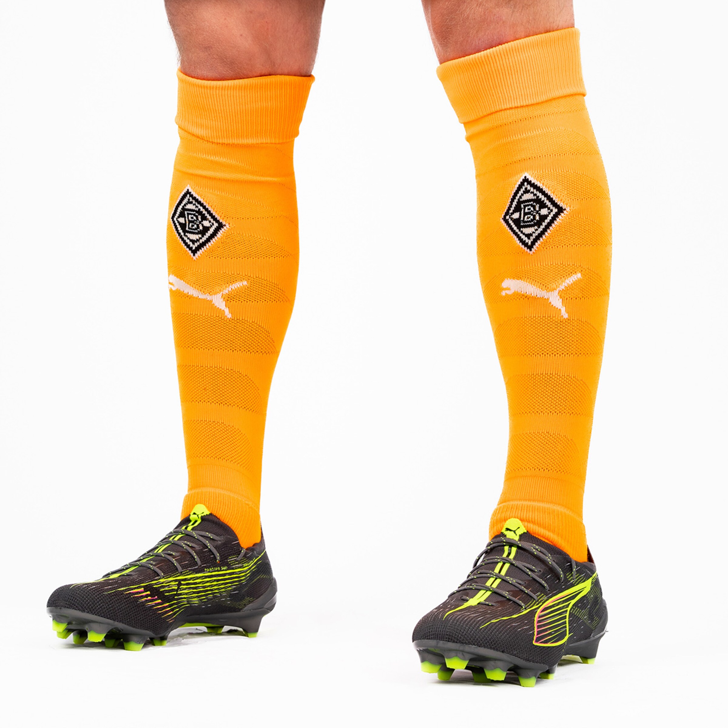 Fußballspieler trägt orangefarbene Socken mit Borussia Mönchengladbach-Logo und PUMA-Symbolen.