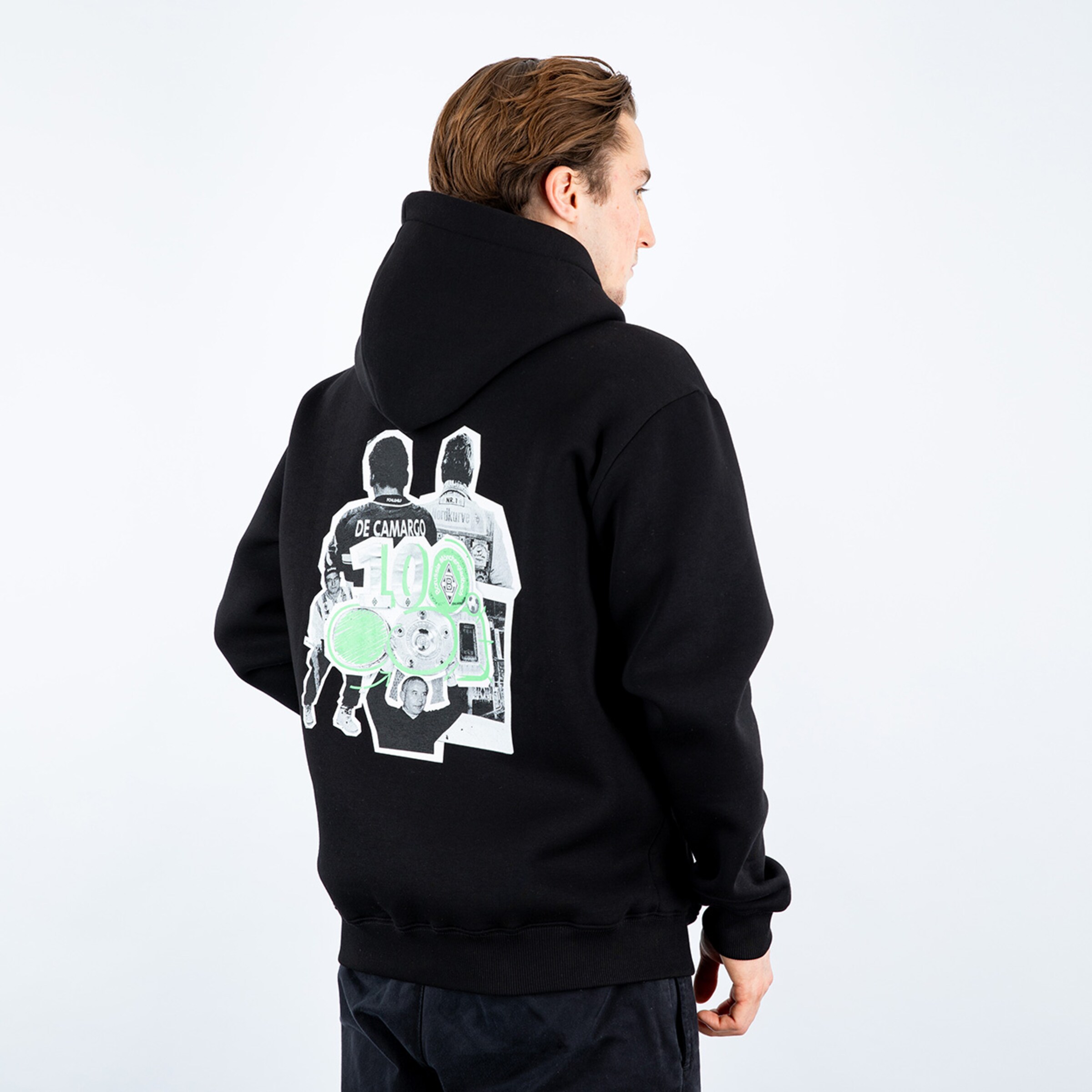 Rückansicht eines Mannes in einem schwarzen Hoodie mit großem Grafikprint auf dem Rücken vor weißem Hintergrund.