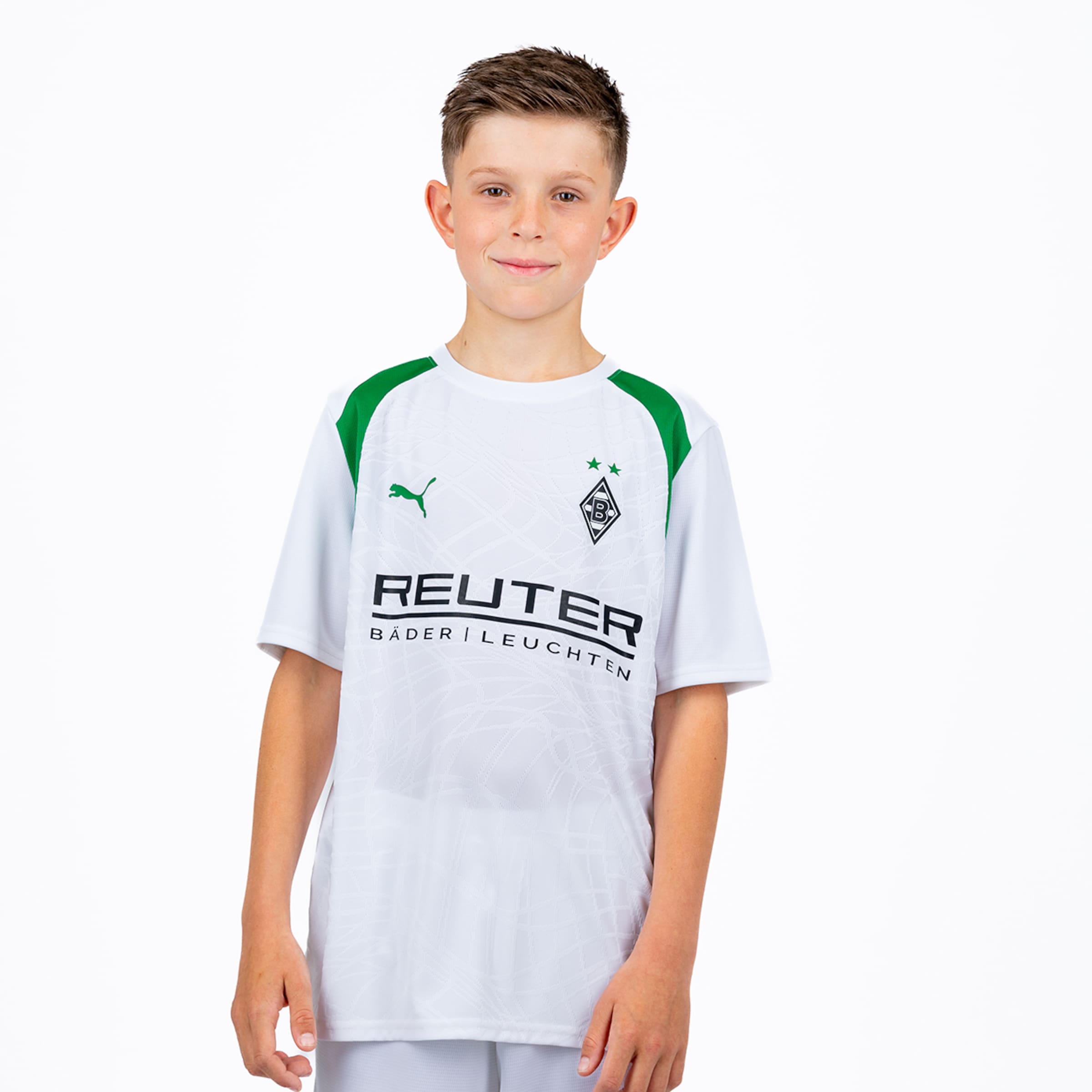 Young boy in white Borussia Mönchengladbach football jersey with green shoulders, Puma logo, and REUTER sponsor. He smiles faintly against a white background.