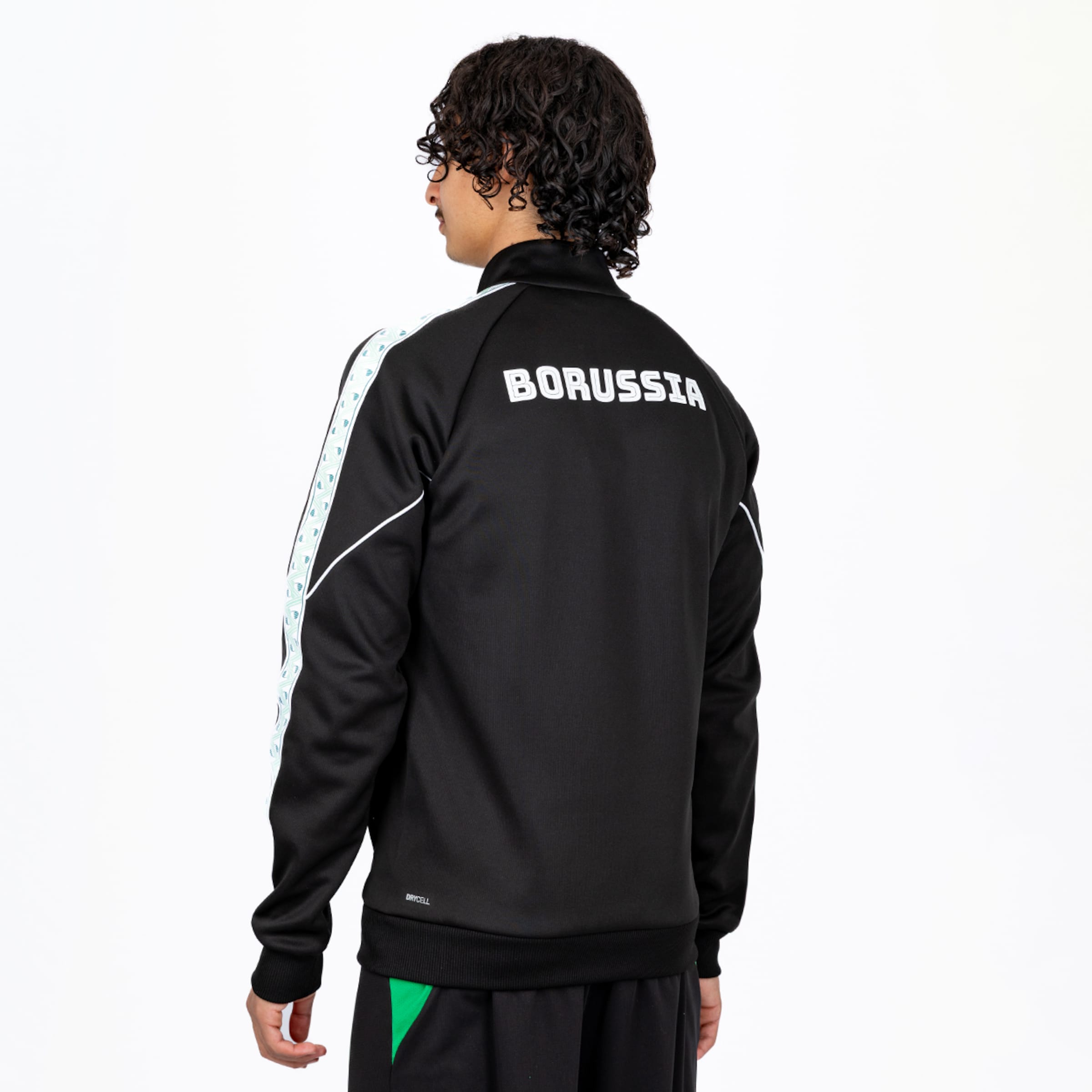 Rückansicht eines Mannes in schwarzer Trainingsjacke mit weißem „BORUSSIA“-Schriftzug und gemusterten Ärmelstreifen.