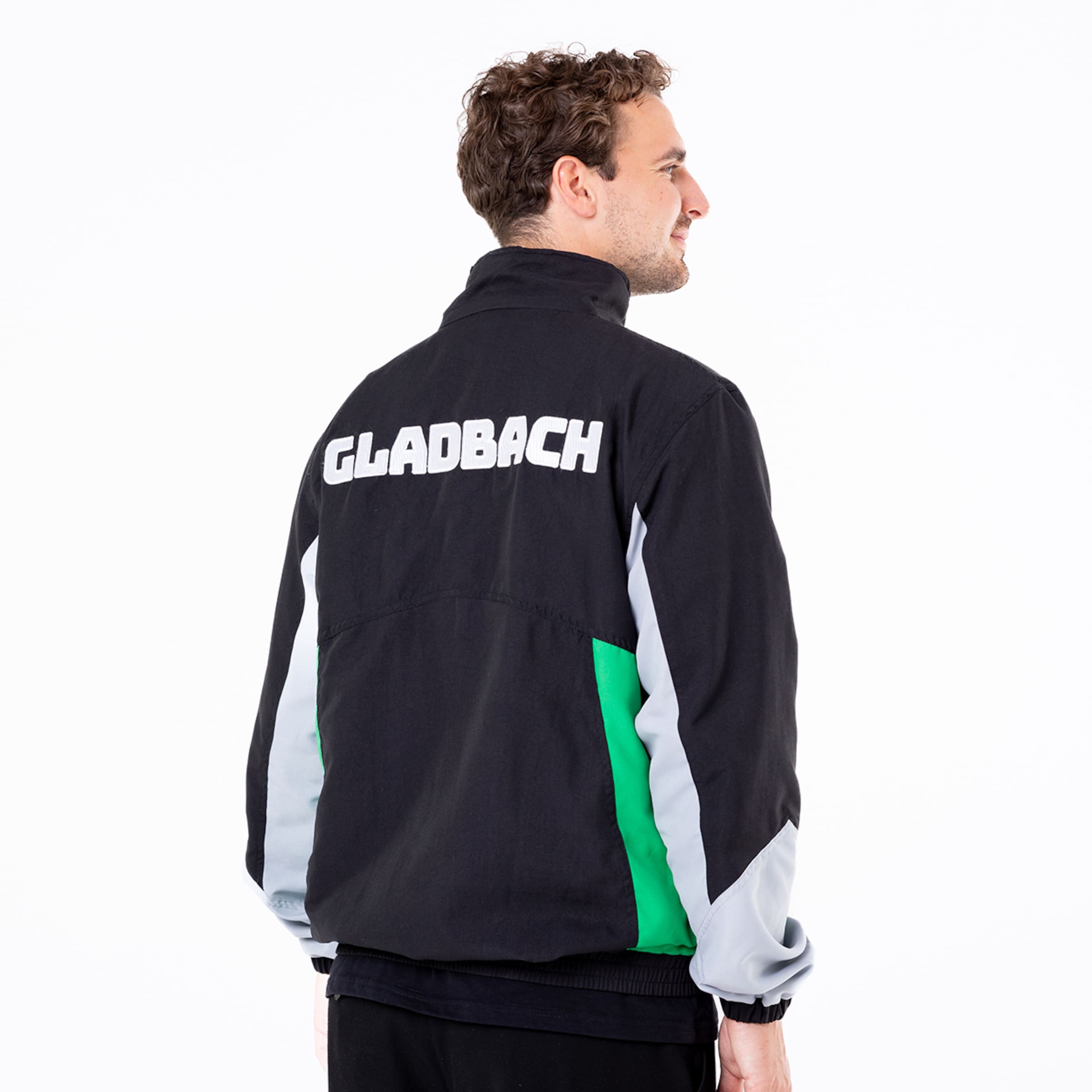 Junger Mann trägt schwarze Jacke mit GLADBACH auf dem Rücken zwei Farbfelder in grün und grau.