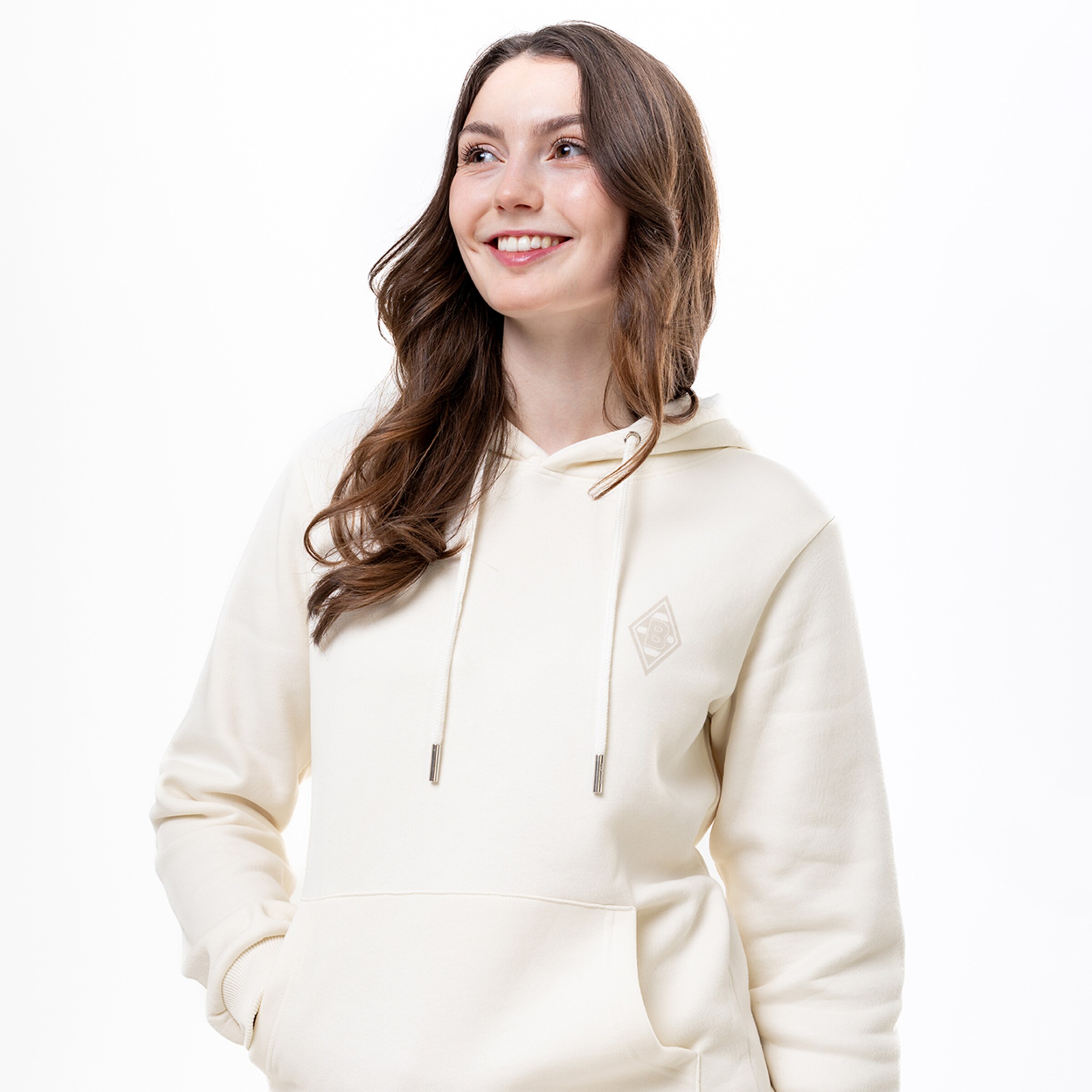 Frau mit braunen Haaren trägt einen hellen Kapuzenpullover und lächelt.
