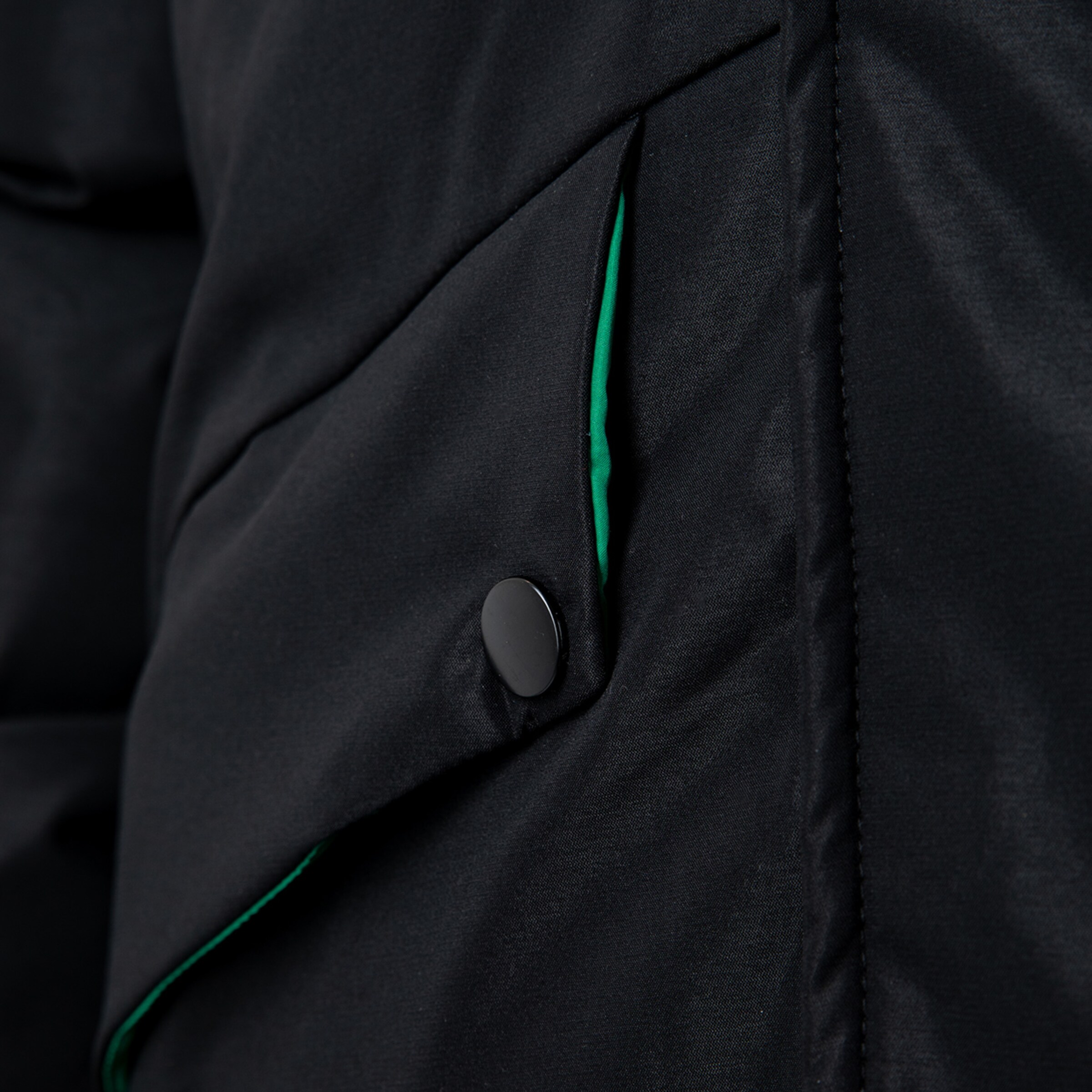 Nahaufnahme eines schwarzen Jackets mit einer grünen Innentasche und Knopf.