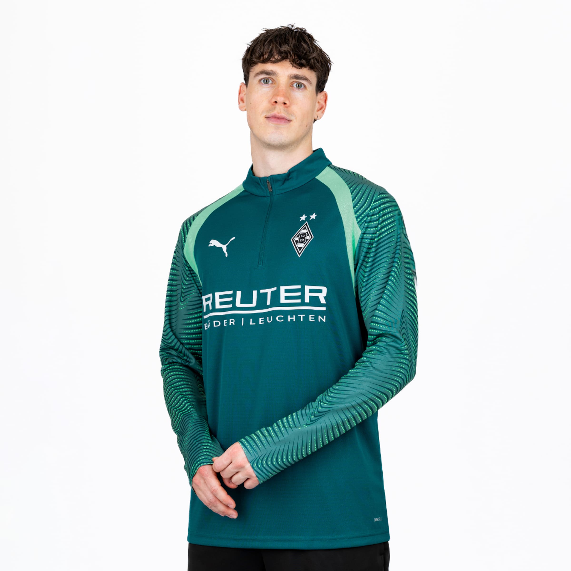 Ein Mann im grünen Langarm-Sportshirt mit Puma-, Borussia Mönchengladbach- und REUTER-Logos steht vor weißem Hintergrund.