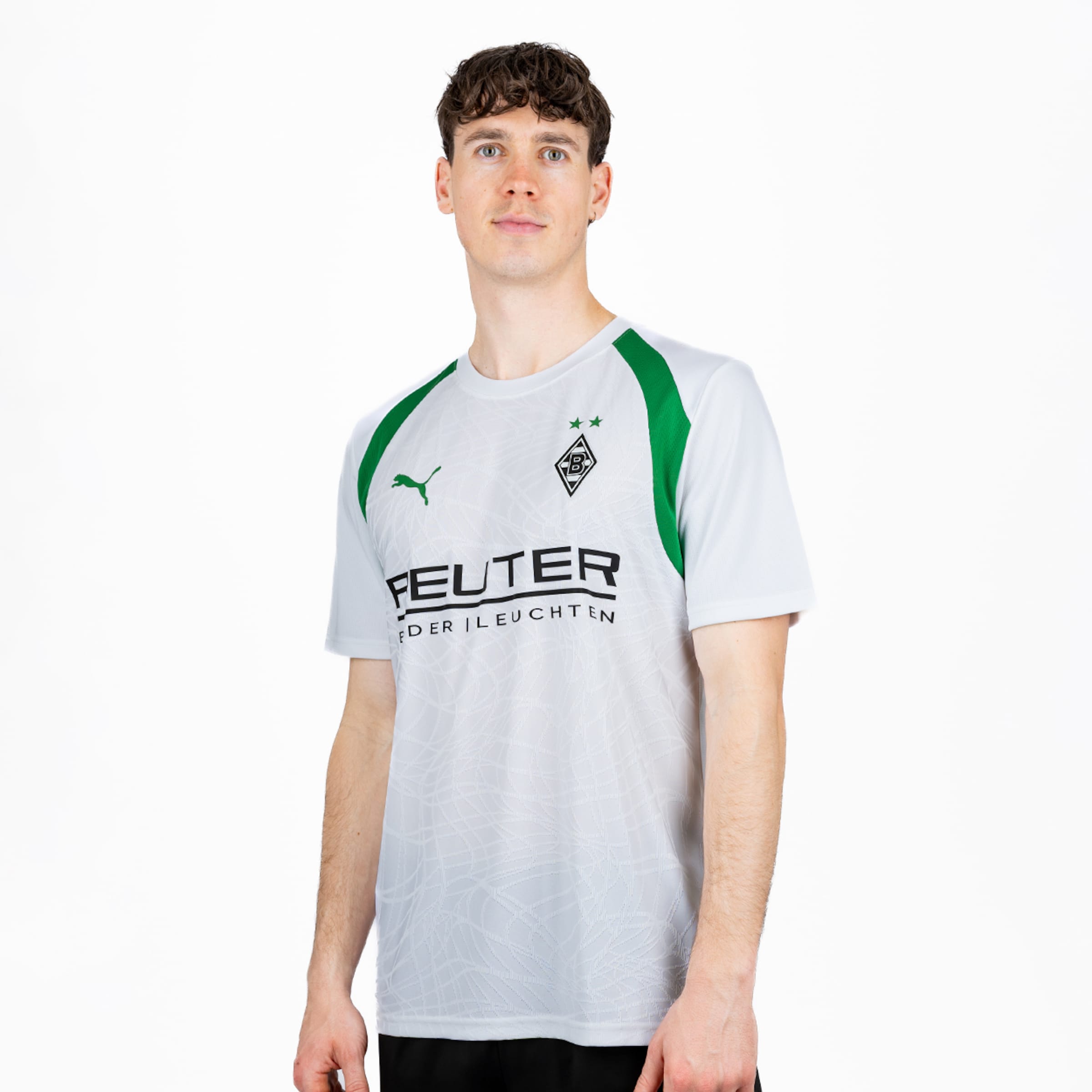 Ein Mann trägt ein weißes Fußballtrikot mit grünen Schulterstreifen, Puma-Logo, Borussia Mönchengladbach-Wappen (zwei Sterne) und 'FEUTER'-Sponsor. Er blickt auf einem weißen Hintergrund nach vorne.
