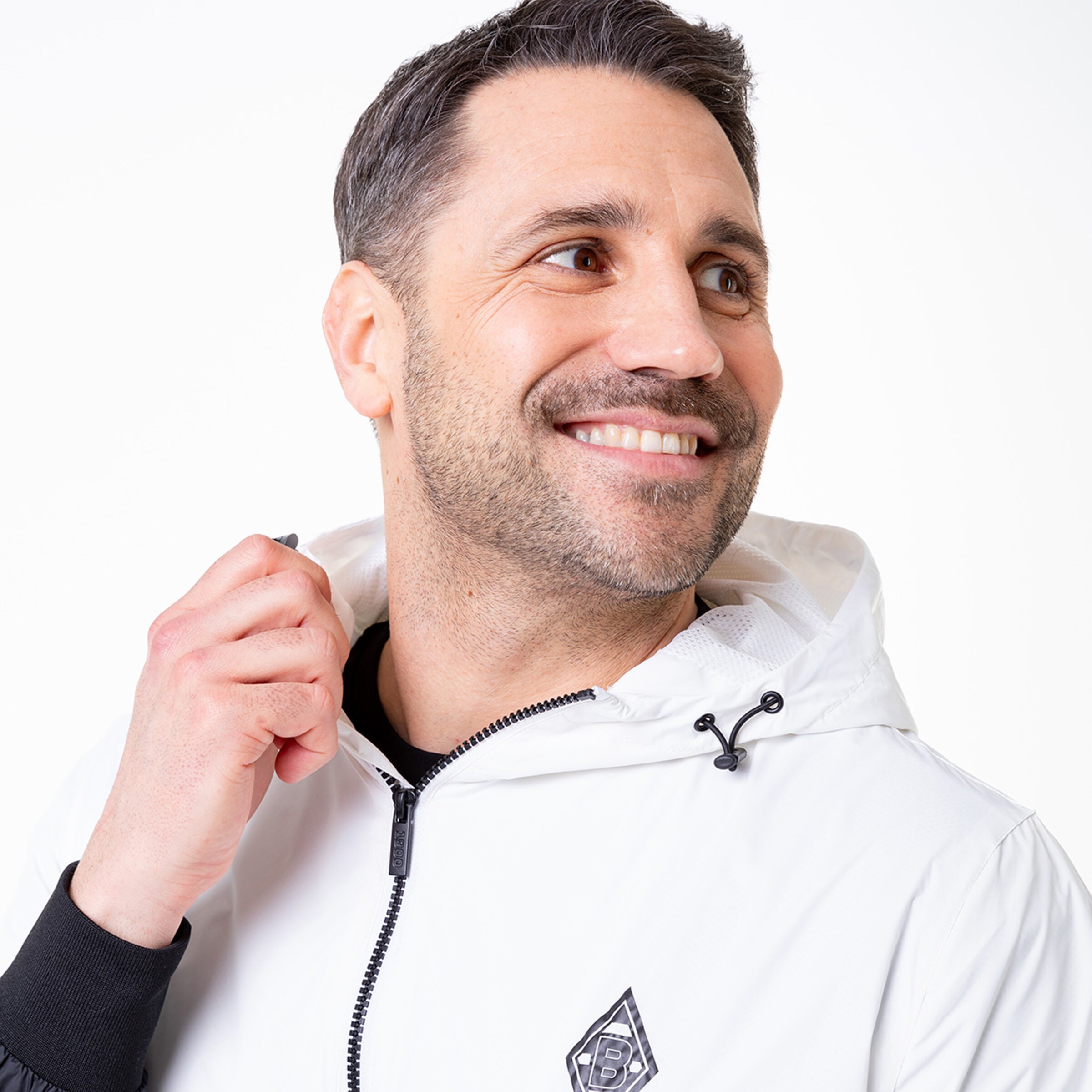 A man smiles while wearing a white hooded jacket.