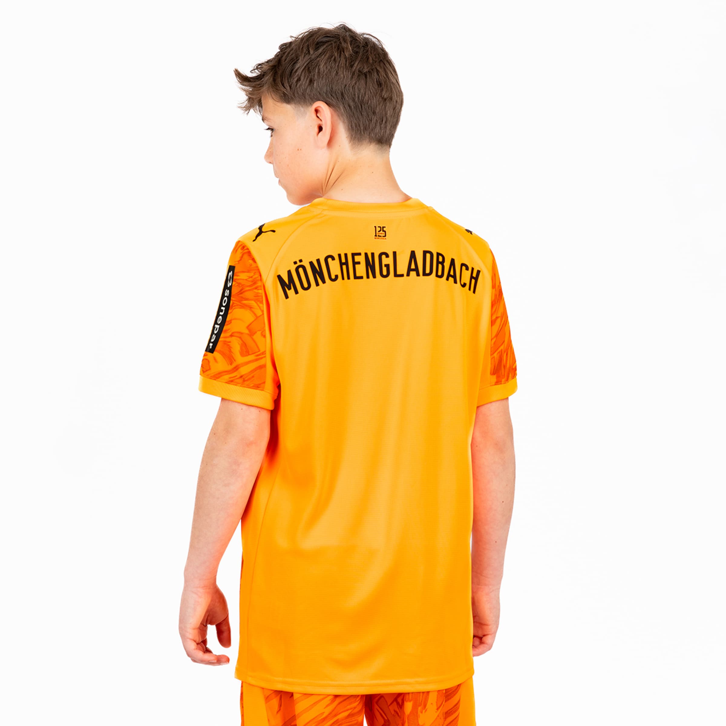 Ein Junge trägt ein orangefarbenes Fußballtrikot mit der Aufschrift MÖNCHENGLADBACH auf dem Rücken.