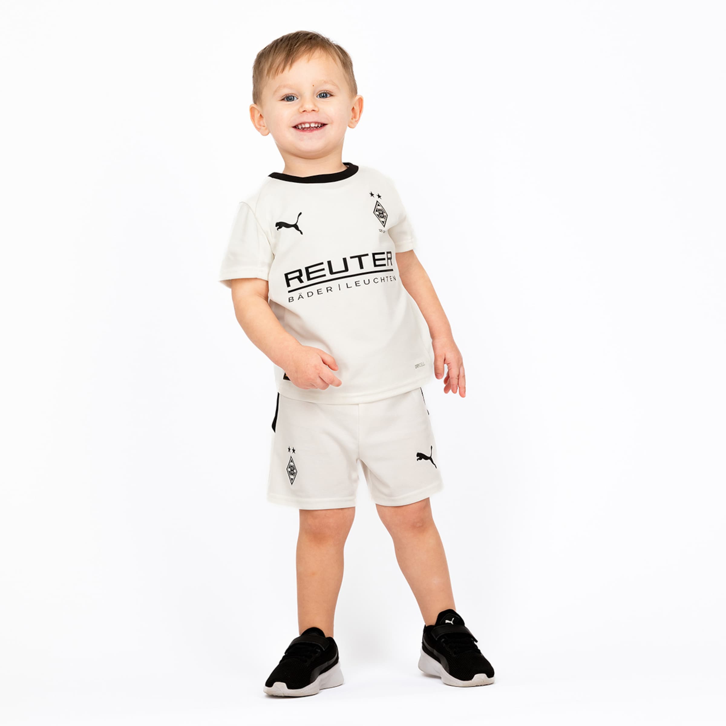 Ein lächelnder Junge trägt das Heimtrikot von Borussia Mönchengladbach in Weiß mit schwarzer Schrift.