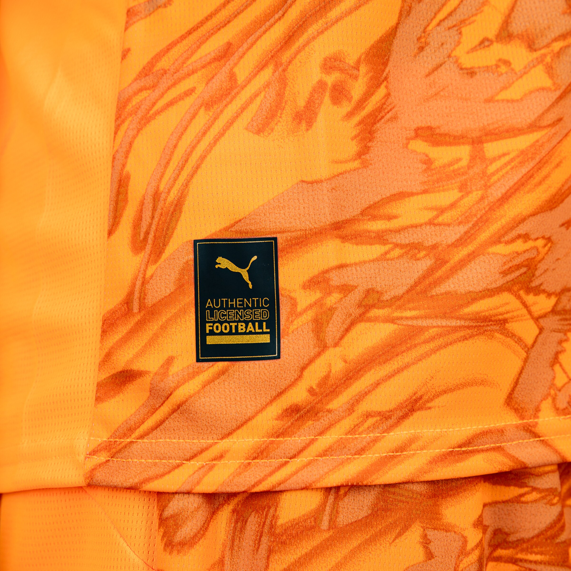 Detailansicht eines orangen Fußballtrikots mit einem Puma-Label AUTHENTIC LICENCED FOOTBALL.