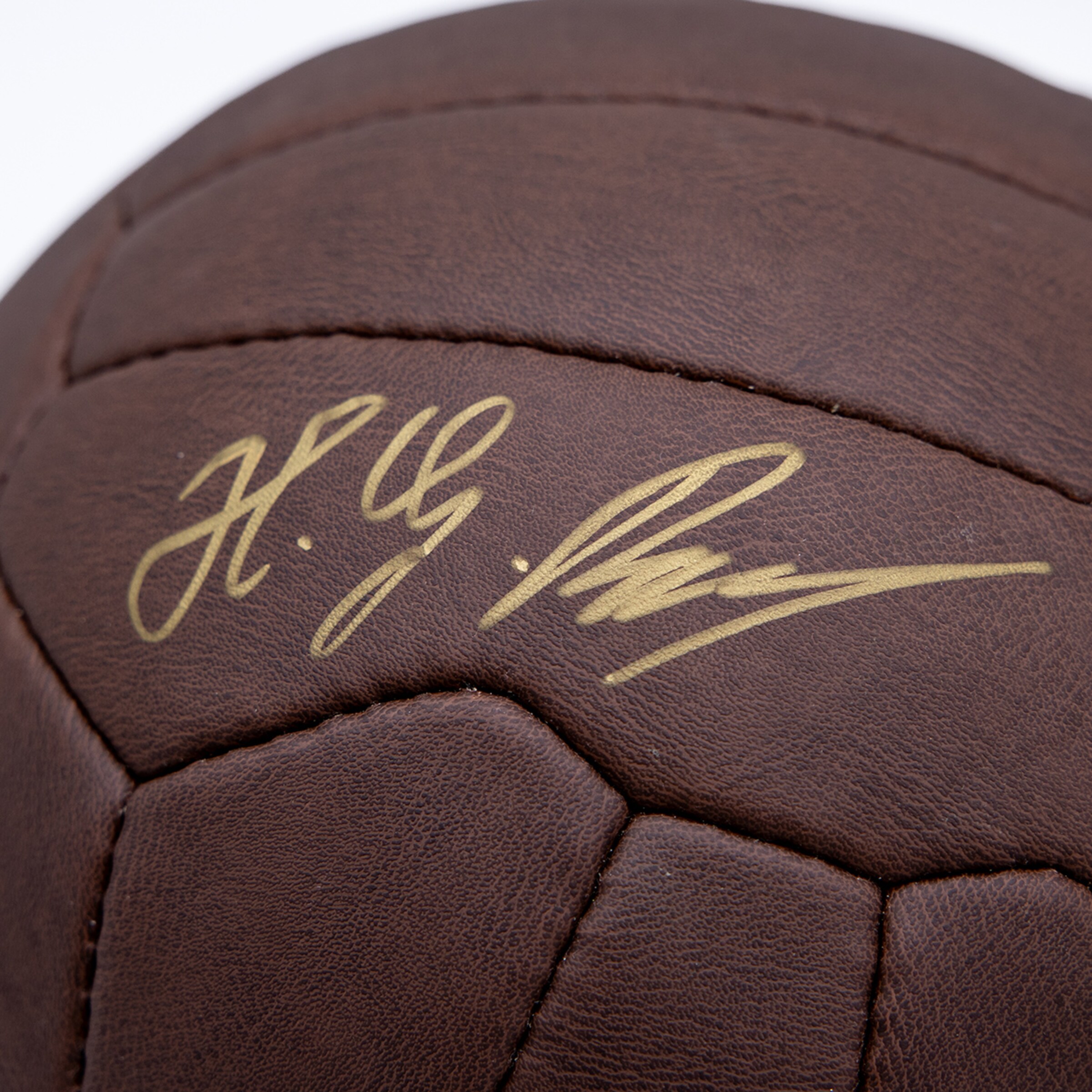 Close-up of a vintage-style brown leather soccer ball with a golden signature.