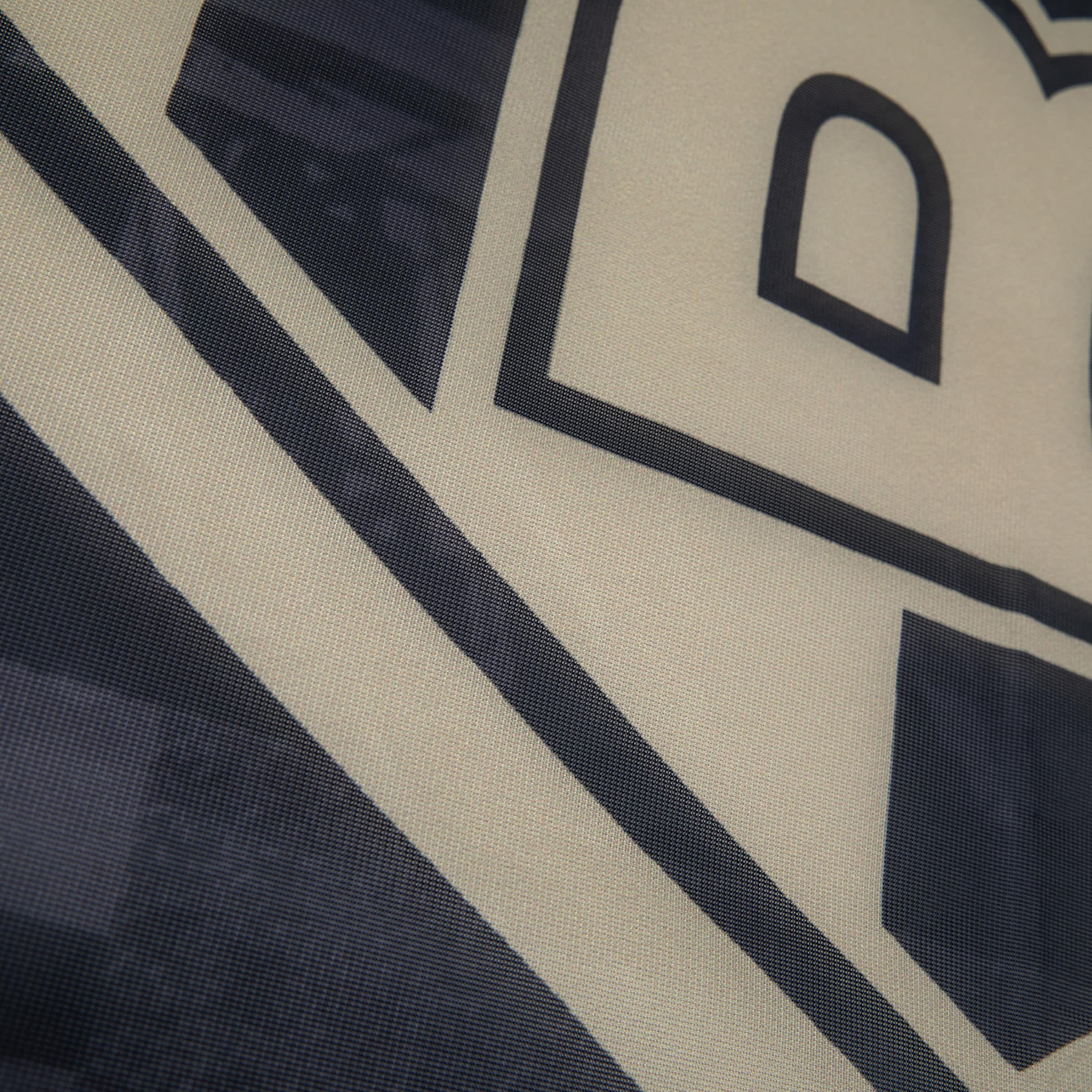 Nahaufnahme eines bedruckten Stoffes mit einem grafischen Logo in Beige und Dunkelblau. Die gewebte Struktur und Linienführung sind erkennbar.