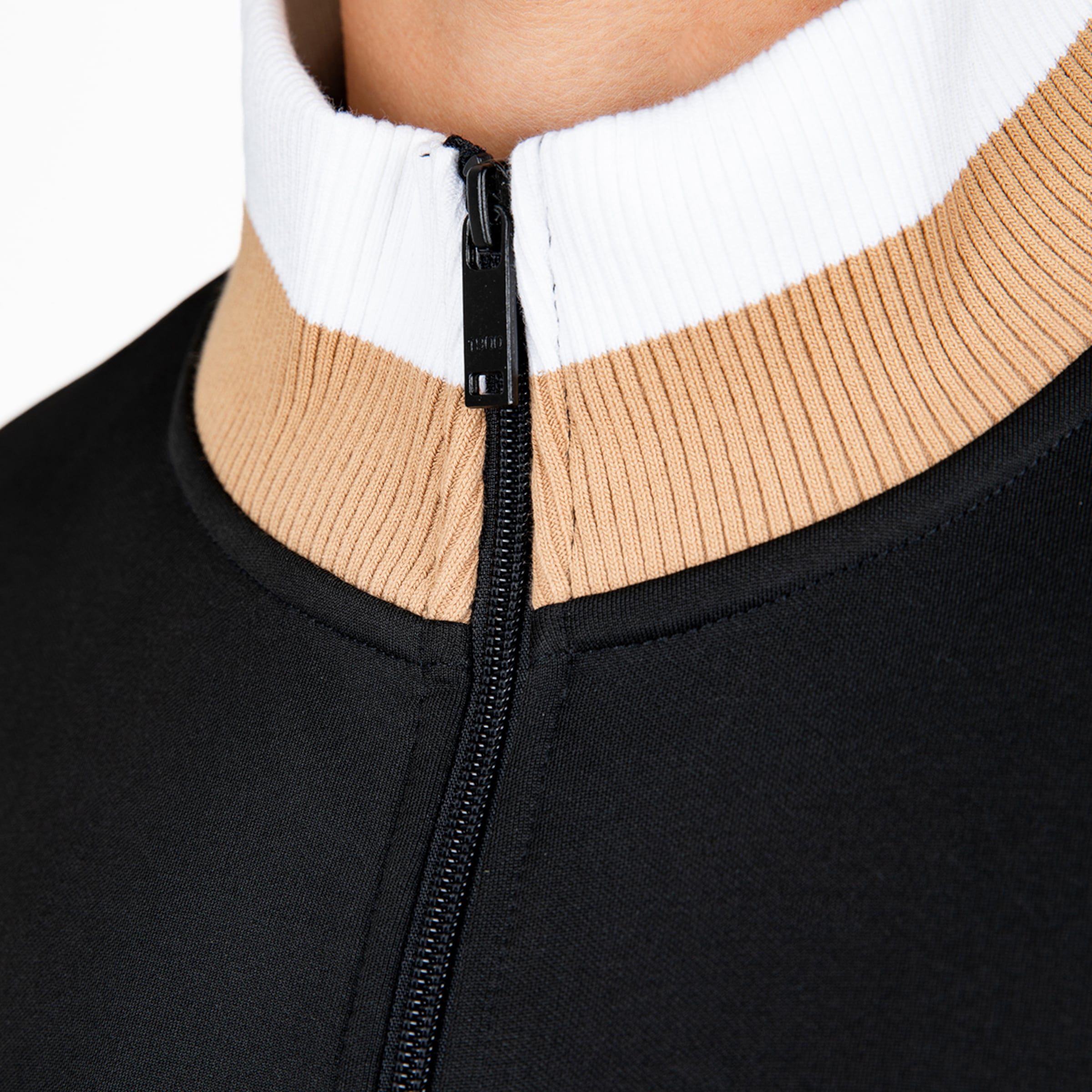Nahaufnahme eines schwarzen Oberteils mit Reißverschluss und gestreiftem Rippstrick-Kragen in Weiß und Beige.