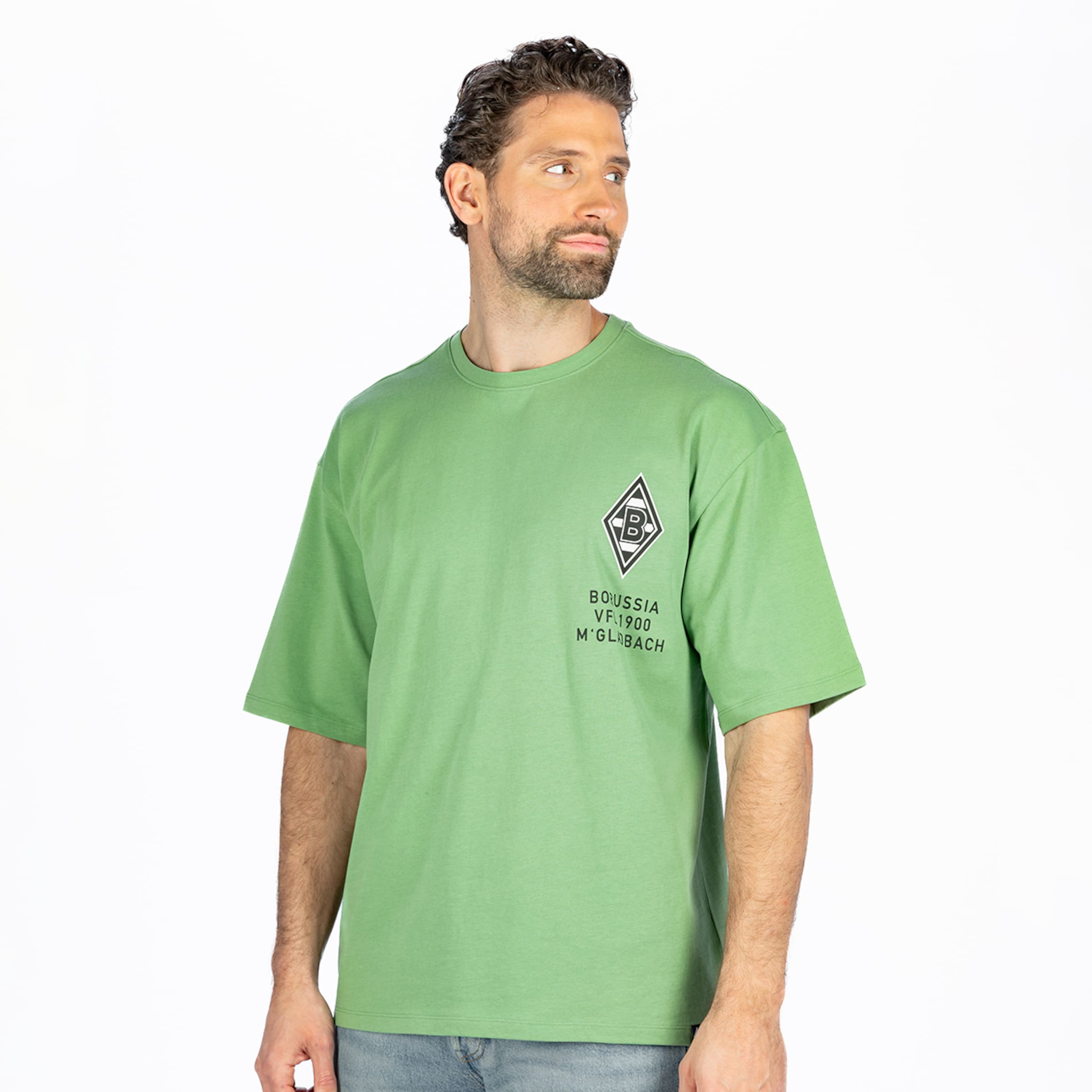 A man with dark, curly hair and a beard wears a light green t-shirt featuring a black and white diamond-shaped logo with a 'B' and the text "BOUSSIA VF 1900 M'GLADBACH". He is looking to his right, against a white background.